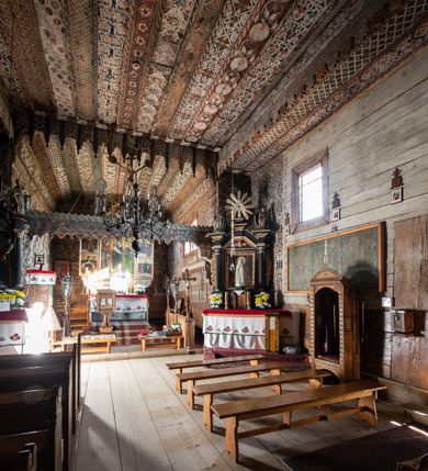 Zdjęcie nr 11: Orientowany, jednoprzestrzenny, nawa na rzucie prostokąta, z węższym, prostokątnym prezbiterium, przy którym od północy wąska zakrystia. Od zachodu przy nawie wieża na rzucie kwadratu, od południa kruchta. Wnętrze nakryte stropem, w nawie z zaskrzynieniem. Portale zachodni i do zakrystii ostrołukowe, fazowane; portal południowy zamknięty łukiem kotarowym. Okna prostokątne, w prezbiterium od południa okno bliźnie, od wschodu zamknięte łukiem kotarowym.  Wokół podcienia, obecnie zaszalowane. Więźba dachowa jętkowa, ze znakami montażowymi.  Dach nad nawą i prezbiterium jednokalenicowy, dwuspadowy, nad nawą z połaciami przedłużonymi na zaskrzynienia i od północy nad zakrystię. Na kalenicy wieżyczka na sygnaturkę z baniastym hełmem.  Wieża o ścianach pochyłych, z nadwieszoną izbicą, zwieńczona ostrosłupowym hełmem. Wokół kościoła ogrodzenie belek układanych na zrąb, z dwiema bramkami. 