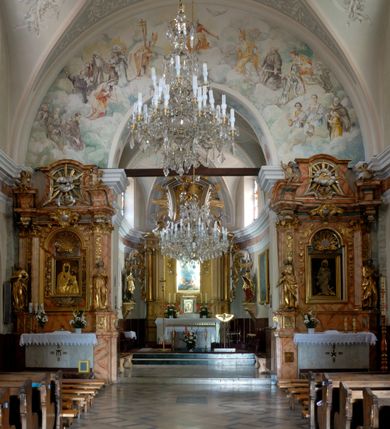 Zdjęcie nr 6: Kościół murowany, orientowany, jednonawowy (z dodatkową przestrzenią od południa powstałą w wyniku połączenia trzech kaplic), z półkoliście zamkniętym prezbiterium, z prostokątną zakrystią od północy, z kruchtą na osi nawy głównej oraz drugą od północy; między zakrystią a kruchtą północną babiniec. 
Nawa szersza od prezbiterium, prostokątna, trójprzęsłowa, ze sklepieniem kolebkowym z lunetami na gurtach. Od zachodu chór muzyczny wsparty na kolumnach. Ściany nawy podzielone zdwojonymi pilastrami, między którymi nisze arkadowe, od południa półokrągłe arkady łączące nawę główną z nawą boczną. Partię ścian od sklepienia oddziela pełne belkowanie wyłamane na osi pilastrów, które jest kontynuowane w przekrytym sklepieniem kolebkowym z lunetami prezbiterium.  
W partii przyziemia oraz sklepienia prostokątne okna w rozglifionych obramieniach zamkniętych łukiem odcinkowym, na osi prezbiterium owalne. Od zachodu oraz od południa drzwi zamknięte łukiem odcinkowym. 
Fasada trójosiowa, dwukondygnacyjna, zwieńczona trójkątnym przyczółkiem, poprzedzona jednokondygnacyjną kruchtą, do której wchodzi się po sześciostopniowych schodach. Osie rozdzielone są pojedynczymi lub zdwojonymi pilastrami, kondygnacje dzieli bogato profilowane belkowanie. W kruchcie drzwi o wykroju prostokąta zamknięte łukiem odcinkowym, okna w osiach bocznych o identycznym jak drzwi wykroju; okulus w szczycie. W osi środkowej drugiej kondygnacji fasady okno prostokątne, zamknięte łukiem odcinkowym, a u szczytu okulus. 
Na elewacjach kontynuowany jest gzyms oddzielający drugą kondygnację i partię dachu, pionowe podziały utworzone zostały przez lizeny. 
Nawa główna oraz kruchty nakryte dachami dwuspadowymi, część nawy bocznej, zakrystia oraz babiniec jednospadowymi, druga część nawy bocznej trójspadowym, zakrystia dwuspadowym zamkniętym półkoliście. Dwie wieżyczki na sygnaturki: jedna nad nawą główną, druga, mniejsza nad prezbiterium. Obie przeprute arkadami, zwieńczone kopułami z kulą i krzyżem. 
Do najważniejszych elementów wyposażenia należą: ołtarz główny późnobarokowy z obrazem Przemienienia Pańskiego przywieziony z Rzymu w 1723 roku, dwa regencyjne ołtarze boczne z barokowymi obrazami Matki Boskiej z Dzieciątkiem oraz św. Katarzyny, oba ozdobione sukienkami oraz obraz z przedstawieniem św. Józefa, pochodzący z trzeciego ołtarza wisi teraz na ścianie nawy głównej. 
