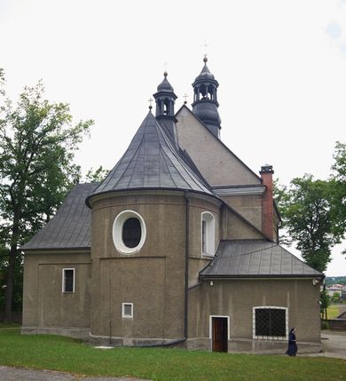 Zdjęcie nr 5: Kościół murowany, orientowany, jednonawowy (z dodatkową przestrzenią od południa powstałą w wyniku połączenia trzech kaplic), z półkoliście zamkniętym prezbiterium, z prostokątną zakrystią od północy, z kruchtą na osi nawy głównej oraz drugą od północy; między zakrystią a kruchtą północną babiniec. 
Nawa szersza od prezbiterium, prostokątna, trójprzęsłowa, ze sklepieniem kolebkowym z lunetami na gurtach. Od zachodu chór muzyczny wsparty na kolumnach. Ściany nawy podzielone zdwojonymi pilastrami, między którymi nisze arkadowe, od południa półokrągłe arkady łączące nawę główną z nawą boczną. Partię ścian od sklepienia oddziela pełne belkowanie wyłamane na osi pilastrów, które jest kontynuowane w przekrytym sklepieniem kolebkowym z lunetami prezbiterium.  
W partii przyziemia oraz sklepienia prostokątne okna w rozglifionych obramieniach zamkniętych łukiem odcinkowym, na osi prezbiterium owalne. Od zachodu oraz od południa drzwi zamknięte łukiem odcinkowym. 
Fasada trójosiowa, dwukondygnacyjna, zwieńczona trójkątnym przyczółkiem, poprzedzona jednokondygnacyjną kruchtą, do której wchodzi się po sześciostopniowych schodach. Osie rozdzielone są pojedynczymi lub zdwojonymi pilastrami, kondygnacje dzieli bogato profilowane belkowanie. W kruchcie drzwi o wykroju prostokąta zamknięte łukiem odcinkowym, okna w osiach bocznych o identycznym jak drzwi wykroju; okulus w szczycie. W osi środkowej drugiej kondygnacji fasady okno prostokątne, zamknięte łukiem odcinkowym, a u szczytu okulus. 
Na elewacjach kontynuowany jest gzyms oddzielający drugą kondygnację i partię dachu, pionowe podziały utworzone zostały przez lizeny. 
Nawa główna oraz kruchty nakryte dachami dwuspadowymi, część nawy bocznej, zakrystia oraz babiniec jednospadowymi, druga część nawy bocznej trójspadowym, zakrystia dwuspadowym zamkniętym półkoliście. Dwie wieżyczki na sygnaturki: jedna nad nawą główną, druga, mniejsza nad prezbiterium. Obie przeprute arkadami, zwieńczone kopułami z kulą i krzyżem. 
Do najważniejszych elementów wyposażenia należą: ołtarz główny późnobarokowy z obrazem Przemienienia Pańskiego przywieziony z Rzymu w 1723 roku, dwa regencyjne ołtarze boczne z barokowymi obrazami Matki Boskiej z Dzieciątkiem oraz św. Katarzyny, oba ozdobione sukienkami oraz obraz z przedstawieniem św. Józefa, pochodzący z trzeciego ołtarza wisi teraz na ścianie nawy głównej. 
