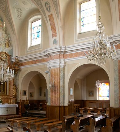 Zdjęcie nr 7: Kościół murowany, orientowany, jednonawowy (z dodatkową przestrzenią od południa powstałą w wyniku połączenia trzech kaplic), z półkoliście zamkniętym prezbiterium, z prostokątną zakrystią od północy, z kruchtą na osi nawy głównej oraz drugą od północy; między zakrystią a kruchtą północną babiniec. 
Nawa szersza od prezbiterium, prostokątna, trójprzęsłowa, ze sklepieniem kolebkowym z lunetami na gurtach. Od zachodu chór muzyczny wsparty na kolumnach. Ściany nawy podzielone zdwojonymi pilastrami, między którymi nisze arkadowe, od południa półokrągłe arkady łączące nawę główną z nawą boczną. Partię ścian od sklepienia oddziela pełne belkowanie wyłamane na osi pilastrów, które jest kontynuowane w przekrytym sklepieniem kolebkowym z lunetami prezbiterium.  
W partii przyziemia oraz sklepienia prostokątne okna w rozglifionych obramieniach zamkniętych łukiem odcinkowym, na osi prezbiterium owalne. Od zachodu oraz od południa drzwi zamknięte łukiem odcinkowym. 
Fasada trójosiowa, dwukondygnacyjna, zwieńczona trójkątnym przyczółkiem, poprzedzona jednokondygnacyjną kruchtą, do której wchodzi się po sześciostopniowych schodach. Osie rozdzielone są pojedynczymi lub zdwojonymi pilastrami, kondygnacje dzieli bogato profilowane belkowanie. W kruchcie drzwi o wykroju prostokąta zamknięte łukiem odcinkowym, okna w osiach bocznych o identycznym jak drzwi wykroju; okulus w szczycie. W osi środkowej drugiej kondygnacji fasady okno prostokątne, zamknięte łukiem odcinkowym, a u szczytu okulus. 
Na elewacjach kontynuowany jest gzyms oddzielający drugą kondygnację i partię dachu, pionowe podziały utworzone zostały przez lizeny. 
Nawa główna oraz kruchty nakryte dachami dwuspadowymi, część nawy bocznej, zakrystia oraz babiniec jednospadowymi, druga część nawy bocznej trójspadowym, zakrystia dwuspadowym zamkniętym półkoliście. Dwie wieżyczki na sygnaturki: jedna nad nawą główną, druga, mniejsza nad prezbiterium. Obie przeprute arkadami, zwieńczone kopułami z kulą i krzyżem. 
Do najważniejszych elementów wyposażenia należą: ołtarz główny późnobarokowy z obrazem Przemienienia Pańskiego przywieziony z Rzymu w 1723 roku, dwa regencyjne ołtarze boczne z barokowymi obrazami Matki Boskiej z Dzieciątkiem oraz św. Katarzyny, oba ozdobione sukienkami oraz obraz z przedstawieniem św. Józefa, pochodzący z trzeciego ołtarza wisi teraz na ścianie nawy głównej. 
