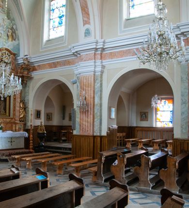 Zdjęcie nr 14: Kościół murowany, orientowany, jednonawowy (z dodatkową przestrzenią od południa powstałą w wyniku połączenia trzech kaplic), z półkoliście zamkniętym prezbiterium, z prostokątną zakrystią od północy, z kruchtą na osi nawy głównej oraz drugą od północy; między zakrystią a kruchtą północną babiniec. 
Nawa szersza od prezbiterium, prostokątna, trójprzęsłowa, ze sklepieniem kolebkowym z lunetami na gurtach. Od zachodu chór muzyczny wsparty na kolumnach. Ściany nawy podzielone zdwojonymi pilastrami, między którymi nisze arkadowe, od południa półokrągłe arkady łączące nawę główną z nawą boczną. Partię ścian od sklepienia oddziela pełne belkowanie wyłamane na osi pilastrów, które jest kontynuowane w przekrytym sklepieniem kolebkowym z lunetami prezbiterium.  
W partii przyziemia oraz sklepienia prostokątne okna w rozglifionych obramieniach zamkniętych łukiem odcinkowym, na osi prezbiterium owalne. Od zachodu oraz od południa drzwi zamknięte łukiem odcinkowym. 
Fasada trójosiowa, dwukondygnacyjna, zwieńczona trójkątnym przyczółkiem, poprzedzona jednokondygnacyjną kruchtą, do której wchodzi się po sześciostopniowych schodach. Osie rozdzielone są pojedynczymi lub zdwojonymi pilastrami, kondygnacje dzieli bogato profilowane belkowanie. W kruchcie drzwi o wykroju prostokąta zamknięte łukiem odcinkowym, okna w osiach bocznych o identycznym jak drzwi wykroju; okulus w szczycie. W osi środkowej drugiej kondygnacji fasady okno prostokątne, zamknięte łukiem odcinkowym, a u szczytu okulus. 
Na elewacjach kontynuowany jest gzyms oddzielający drugą kondygnację i partię dachu, pionowe podziały utworzone zostały przez lizeny. 
Nawa główna oraz kruchty nakryte dachami dwuspadowymi, część nawy bocznej, zakrystia oraz babiniec jednospadowymi, druga część nawy bocznej trójspadowym, zakrystia dwuspadowym zamkniętym półkoliście. Dwie wieżyczki na sygnaturki: jedna nad nawą główną, druga, mniejsza nad prezbiterium. Obie przeprute arkadami, zwieńczone kopułami z kulą i krzyżem. 
Do najważniejszych elementów wyposażenia należą: ołtarz główny późnobarokowy z obrazem Przemienienia Pańskiego przywieziony z Rzymu w 1723 roku, dwa regencyjne ołtarze boczne z barokowymi obrazami Matki Boskiej z Dzieciątkiem oraz św. Katarzyny, oba ozdobione sukienkami oraz obraz z przedstawieniem św. Józefa, pochodzący z trzeciego ołtarza wisi teraz na ścianie nawy głównej. 
