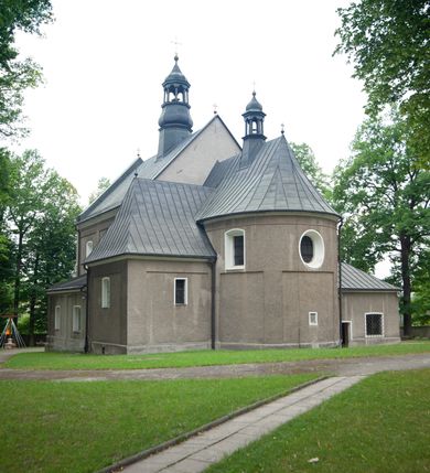 Zdjęcie nr 13: Kościół murowany, orientowany, jednonawowy (z dodatkową przestrzenią od południa powstałą w wyniku połączenia trzech kaplic), z półkoliście zamkniętym prezbiterium, z prostokątną zakrystią od północy, z kruchtą na osi nawy głównej oraz drugą od północy; między zakrystią a kruchtą północną babiniec. 
Nawa szersza od prezbiterium, prostokątna, trójprzęsłowa, ze sklepieniem kolebkowym z lunetami na gurtach. Od zachodu chór muzyczny wsparty na kolumnach. Ściany nawy podzielone zdwojonymi pilastrami, między którymi nisze arkadowe, od południa półokrągłe arkady łączące nawę główną z nawą boczną. Partię ścian od sklepienia oddziela pełne belkowanie wyłamane na osi pilastrów, które jest kontynuowane w przekrytym sklepieniem kolebkowym z lunetami prezbiterium.  
W partii przyziemia oraz sklepienia prostokątne okna w rozglifionych obramieniach zamkniętych łukiem odcinkowym, na osi prezbiterium owalne. Od zachodu oraz od południa drzwi zamknięte łukiem odcinkowym. 
Fasada trójosiowa, dwukondygnacyjna, zwieńczona trójkątnym przyczółkiem, poprzedzona jednokondygnacyjną kruchtą, do której wchodzi się po sześciostopniowych schodach. Osie rozdzielone są pojedynczymi lub zdwojonymi pilastrami, kondygnacje dzieli bogato profilowane belkowanie. W kruchcie drzwi o wykroju prostokąta zamknięte łukiem odcinkowym, okna w osiach bocznych o identycznym jak drzwi wykroju; okulus w szczycie. W osi środkowej drugiej kondygnacji fasady okno prostokątne, zamknięte łukiem odcinkowym, a u szczytu okulus. 
Na elewacjach kontynuowany jest gzyms oddzielający drugą kondygnację i partię dachu, pionowe podziały utworzone zostały przez lizeny. 
Nawa główna oraz kruchty nakryte dachami dwuspadowymi, część nawy bocznej, zakrystia oraz babiniec jednospadowymi, druga część nawy bocznej trójspadowym, zakrystia dwuspadowym zamkniętym półkoliście. Dwie wieżyczki na sygnaturki: jedna nad nawą główną, druga, mniejsza nad prezbiterium. Obie przeprute arkadami, zwieńczone kopułami z kulą i krzyżem. 
Do najważniejszych elementów wyposażenia należą: ołtarz główny późnobarokowy z obrazem Przemienienia Pańskiego przywieziony z Rzymu w 1723 roku, dwa regencyjne ołtarze boczne z barokowymi obrazami Matki Boskiej z Dzieciątkiem oraz św. Katarzyny, oba ozdobione sukienkami oraz obraz z przedstawieniem św. Józefa, pochodzący z trzeciego ołtarza wisi teraz na ścianie nawy głównej. 
