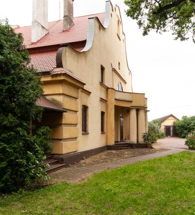 Zdjęcie nr 2: Plebania jest usytuowana po południowej stronie kościoła; poza obrębem ogrodzenia. Budyneka zwrócony frontem ku północy, parterowy z mieszkalnym poddaszem, częściowo podpiwniczony. Na rzucie szerokiego prostokąta, układ wnętrza osiowy, w ogólnej dyspozycji trójdzielny, dwutraktowy; od zachodu trzytraktowy. Przy elewacji wschodniej niska przybudówka. Na osi budynku od północy sień, od południa salon. W części wschodniej cztery pomieszczenia w tym trzy mieszkalne oraz kancelaria parafialna dostępna osobnym wejściem przez przybudówkę. W części zachodniej sześć pomieszczeń, w tym kuchnia, spiżarnia, sanitariaty, wewnętrzny korytarz oraz nieregularne pomieszczenie klatki schodowej na poddasze. Na poddaszu sześć pomieszczeń. W pomieszczeniach sufity. W salonie bogato zdobiony strop kasetonowy z licznymi inskrypcjami m.in.: łacińskim wersetem, datą budowy – 1922 roku, oraz zapisy dotyczące fundacji kościoła w 1223 roku, założenia kamienia węgielnego odbudowy kościoła po zniszczeniach wojennych w 1923 roku, objęcia rządów nad diecezją kielecką przez arcybiskupa Sapiechę w 1925 roku, oraz wystawienia przy kościele kaplicy Matki Boskiej Bolesnej i budowy plebanii staraniem księdza Boratyńskiego. W pomieszczeniach piece kaflowe; w salonie ozdobny. Elewacje zewnętrze tynkowane na żółto, na cokole, z narożami ujętymi wydatnym boniowaniem. Okna niewielkie zamknięte łukami odcinkowymi, w elewacjach dłuższych boków ponad oknami parteru odcinki gzymsu okapowego. W obu dłuższych elewacjach szerokie szczyty o fantazyjnej, falistej linii z sześcioma kolistymi prześwitami wzdłuż krawędzi; pośrodku po obu stronach duże półkoliste okna, w części środkowej zawierające wyjścia na balkony: frontowy wsparty na czterech kolumnach i tylny nadwieszony, mały, niedokończony. Po bokach okien półkolistych po jednym oknie, ponadto powyżej z obu stron po jednym okienku strychowym; w zwieńczeniu szczytu od północy pusta płycina zamknięta półkoliście. Dach dwuspadowy, łamany, kryty dachówką. 


Inskrypcje ze stropu kasetonowego: Inskrypcje ze stropu kasetonowego: 1) Na ramach kasetonów: COMES SIT IPSE DEUS / INDEQUE MIGRANTI / A(NNO) D(OMINI) 1922 / BENEDICTO QUOQUE MANENTI / SALUS HIC INTRANTI; 2) W płycinach: 1. Wystawienie kaplicy Matki Boskiej Bolesnej i wybudowanie plebanji dla wielu- zgorszeniem, dla wielu - zrozumieniem, dla mnie świętym trudem, jako usprawiedliwienie moje przed Bogiem. Prob(oszcz) Par(afii) Wawrzeńczcyce ks(iądz) Zygmunt Boratyński. 1919-1932; 2. Iwo Odrowąż Biskup Krakowski Fundator Kościoła św. Marji Magdaleny w Wawrzeńczycach 1223.; 3. Książę Adam Stefan Sapieha Arcybiskup – Metropolita Krakowski objął rządy na parafją Wawrzeńczyce diecezji Kieleckiej 1925 r (oku); 4. J(ego) E(kscelencja) X(iądz) Augustyn Łosiński Biskup Kielecki założył kamień węgielny pod odbudowę kościoła dn(ia) 22 lipca 1923 r(oku) w uroczystość 700lecia kościoła par(afialnego) w Wawrzeńczycach zniszczonego przez wojnę w r(oku) 1914. 1223-1923.