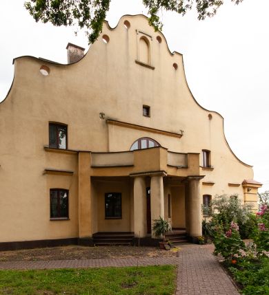 Zdjęcie nr 1: Plebania jest usytuowana po południowej stronie kościoła; poza obrębem ogrodzenia. Budyneka zwrócony frontem ku północy, parterowy z mieszkalnym poddaszem, częściowo podpiwniczony. Na rzucie szerokiego prostokąta, układ wnętrza osiowy, w ogólnej dyspozycji trójdzielny, dwutraktowy; od zachodu trzytraktowy. Przy elewacji wschodniej niska przybudówka. Na osi budynku od północy sień, od południa salon. W części wschodniej cztery pomieszczenia w tym trzy mieszkalne oraz kancelaria parafialna dostępna osobnym wejściem przez przybudówkę. W części zachodniej sześć pomieszczeń, w tym kuchnia, spiżarnia, sanitariaty, wewnętrzny korytarz oraz nieregularne pomieszczenie klatki schodowej na poddasze. Na poddaszu sześć pomieszczeń. W pomieszczeniach sufity. W salonie bogato zdobiony strop kasetonowy z licznymi inskrypcjami m.in.: łacińskim wersetem, datą budowy – 1922 roku, oraz zapisy dotyczące fundacji kościoła w 1223 roku, założenia kamienia węgielnego odbudowy kościoła po zniszczeniach wojennych w 1923 roku, objęcia rządów nad diecezją kielecką przez arcybiskupa Sapiechę w 1925 roku, oraz wystawienia przy kościele kaplicy Matki Boskiej Bolesnej i budowy plebanii staraniem księdza Boratyńskiego. W pomieszczeniach piece kaflowe; w salonie ozdobny. Elewacje zewnętrze tynkowane na żółto, na cokole, z narożami ujętymi wydatnym boniowaniem. Okna niewielkie zamknięte łukami odcinkowymi, w elewacjach dłuższych boków ponad oknami parteru odcinki gzymsu okapowego. W obu dłuższych elewacjach szerokie szczyty o fantazyjnej, falistej linii z sześcioma kolistymi prześwitami wzdłuż krawędzi; pośrodku po obu stronach duże półkoliste okna, w części środkowej zawierające wyjścia na balkony: frontowy wsparty na czterech kolumnach i tylny nadwieszony, mały, niedokończony. Po bokach okien półkolistych po jednym oknie, ponadto powyżej z obu stron po jednym okienku strychowym; w zwieńczeniu szczytu od północy pusta płycina zamknięta półkoliście. Dach dwuspadowy, łamany, kryty dachówką. 


Inskrypcje ze stropu kasetonowego: Inskrypcje ze stropu kasetonowego: 1) Na ramach kasetonów: COMES SIT IPSE DEUS / INDEQUE MIGRANTI / A(NNO) D(OMINI) 1922 / BENEDICTO QUOQUE MANENTI / SALUS HIC INTRANTI; 2) W płycinach: 1. Wystawienie kaplicy Matki Boskiej Bolesnej i wybudowanie plebanji dla wielu- zgorszeniem, dla wielu - zrozumieniem, dla mnie świętym trudem, jako usprawiedliwienie moje przed Bogiem. Prob(oszcz) Par(afii) Wawrzeńczcyce ks(iądz) Zygmunt Boratyński. 1919-1932; 2. Iwo Odrowąż Biskup Krakowski Fundator Kościoła św. Marji Magdaleny w Wawrzeńczycach 1223.; 3. Książę Adam Stefan Sapieha Arcybiskup – Metropolita Krakowski objął rządy na parafją Wawrzeńczyce diecezji Kieleckiej 1925 r (oku); 4. J(ego) E(kscelencja) X(iądz) Augustyn Łosiński Biskup Kielecki założył kamień węgielny pod odbudowę kościoła dn(ia) 22 lipca 1923 r(oku) w uroczystość 700lecia kościoła par(afialnego) w Wawrzeńczycach zniszczonego przez wojnę w r(oku) 1914. 1223-1923.