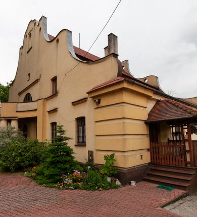 Zdjęcie nr 5: Plebania jest usytuowana po południowej stronie kościoła; poza obrębem ogrodzenia. Budyneka zwrócony frontem ku północy, parterowy z mieszkalnym poddaszem, częściowo podpiwniczony. Na rzucie szerokiego prostokąta, układ wnętrza osiowy, w ogólnej dyspozycji trójdzielny, dwutraktowy; od zachodu trzytraktowy. Przy elewacji wschodniej niska przybudówka. Na osi budynku od północy sień, od południa salon. W części wschodniej cztery pomieszczenia w tym trzy mieszkalne oraz kancelaria parafialna dostępna osobnym wejściem przez przybudówkę. W części zachodniej sześć pomieszczeń, w tym kuchnia, spiżarnia, sanitariaty, wewnętrzny korytarz oraz nieregularne pomieszczenie klatki schodowej na poddasze. Na poddaszu sześć pomieszczeń. W pomieszczeniach sufity. W salonie bogato zdobiony strop kasetonowy z licznymi inskrypcjami m.in.: łacińskim wersetem, datą budowy – 1922 roku, oraz zapisy dotyczące fundacji kościoła w 1223 roku, założenia kamienia węgielnego odbudowy kościoła po zniszczeniach wojennych w 1923 roku, objęcia rządów nad diecezją kielecką przez arcybiskupa Sapiechę w 1925 roku, oraz wystawienia przy kościele kaplicy Matki Boskiej Bolesnej i budowy plebanii staraniem księdza Boratyńskiego. W pomieszczeniach piece kaflowe; w salonie ozdobny. Elewacje zewnętrze tynkowane na żółto, na cokole, z narożami ujętymi wydatnym boniowaniem. Okna niewielkie zamknięte łukami odcinkowymi, w elewacjach dłuższych boków ponad oknami parteru odcinki gzymsu okapowego. W obu dłuższych elewacjach szerokie szczyty o fantazyjnej, falistej linii z sześcioma kolistymi prześwitami wzdłuż krawędzi; pośrodku po obu stronach duże półkoliste okna, w części środkowej zawierające wyjścia na balkony: frontowy wsparty na czterech kolumnach i tylny nadwieszony, mały, niedokończony. Po bokach okien półkolistych po jednym oknie, ponadto powyżej z obu stron po jednym okienku strychowym; w zwieńczeniu szczytu od północy pusta płycina zamknięta półkoliście. Dach dwuspadowy, łamany, kryty dachówką. 


Inskrypcje ze stropu kasetonowego: Inskrypcje ze stropu kasetonowego: 1) Na ramach kasetonów: COMES SIT IPSE DEUS / INDEQUE MIGRANTI / A(NNO) D(OMINI) 1922 / BENEDICTO QUOQUE MANENTI / SALUS HIC INTRANTI; 2) W płycinach: 1. Wystawienie kaplicy Matki Boskiej Bolesnej i wybudowanie plebanji dla wielu- zgorszeniem, dla wielu - zrozumieniem, dla mnie świętym trudem, jako usprawiedliwienie moje przed Bogiem. Prob(oszcz) Par(afii) Wawrzeńczcyce ks(iądz) Zygmunt Boratyński. 1919-1932; 2. Iwo Odrowąż Biskup Krakowski Fundator Kościoła św. Marji Magdaleny w Wawrzeńczycach 1223.; 3. Książę Adam Stefan Sapieha Arcybiskup – Metropolita Krakowski objął rządy na parafją Wawrzeńczyce diecezji Kieleckiej 1925 r (oku); 4. J(ego) E(kscelencja) X(iądz) Augustyn Łosiński Biskup Kielecki założył kamień węgielny pod odbudowę kościoła dn(ia) 22 lipca 1923 r(oku) w uroczystość 700lecia kościoła par(afialnego) w Wawrzeńczycach zniszczonego przez wojnę w r(oku) 1914. 1223-1923.