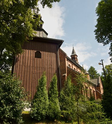 Zdjęcie nr 6: Murowana z cegły, orientowana, trzynawowa bazylika emporowa z prezbiterium zamkniętym trójbocznie. Do jednej czwartej wysokości murów lico kamienne, całość obiega cokół. Fasada dwukondygnacyjna, trójosiowa; oś środkowa wysunięta przed lico muru. Podziały pionowe tworzą dwuuskokowe przypory, poziome gzyms w połowie wysokości osi środkowej. Na osi portal ostrołukowy, uskokowy, flankowany filarami wspartymi na wysokich cokołach. W filarach fragmenty laski. Powyżej wsporniki podtrzymujące wąską archiwoltę otoczoną fryzem arkadowym. Nad otworem drzwiowym tympanon o zarysie łuku ostrego. W zwieńczeniu trójkątny przyczółek, którego ramiona spływają na konsolki oparte na filarach; całość wieńczy krzyż. Ponad portalem dwa okna w uskokowym obramieniu zakończonym łukiem ostrym. Ponad nimi okrągłe okno, wyżej kamienny kartusz z herbem fundatorki. Fasadę wieńczy ząbkowanie i fryz arkadowy. W skrajnych osiach okna ostrołukowe. W dolnym, lewym rogu osi środkowej data: MCMV. Podziały ścian nawy bocznej stanowią trójskokowe przypory; pomiędzy nimi okna ostrołukowe w uskokowych obramieniach. Ponad oknami ząbkowanie, profilowany architraw, fryz i gzyms wsparty na kroksztynach. W partii nawy głównej podział ścian tworzą małe przypory, pomiędzy którymi znajdują się okrągłe okna, ponad nimi fryz arkadowy. W zwieńczeniu kroksztyny. W ścianach zakrystii dwa wąskie, ostrołukowe okna i jedno okrągłe w profilowanych obramieniach. W trójkątnym zwieńczeniu fryz arkadowy ujęty w dwa pasy ząbkowania. Przy zachodniej ścianie południowej zakrystii znajduje się boczne wejście otwarte dwoma ostrołukowymi arkadami, wspartymi na filarze. W górnej partii ozdobione fryzem arkadowym, ząbkowaniem i kroksztynami. Pomiędzy nawą boczną a południową zakrystią okrągła wieżyczka z dwoma kwadratowymi otworami okiennymi. Strona północna analogiczna do południowej, oprócz pomieszczenia między nawą a zakrystią i portalu w pomieszczeniu przy kruchcie. Pomieszczenie z wejściem pomocniczym od strony zachodniej Od północy wąskie okno zamknięte łukiem półkolistym, w narożach ryzality zwieńczone konsolkami z fryzem arkadowym i gzymsem pomiędzy. Portal kamienny, ustawiony na czterech stopniach, ostrołukowy, zwieńczony trójkątnym przyczółkiem z ramionami spływającymi na profilowane konsole. Prezbiterium opięte czterema przyporami dwuuskokowymi. W ścianie wschodniej płycina zakończona łukiem ostrym. W zwieńczeniu fryz arkadowy i gzyms wsparty na kroksztynach. Pomiędzy nawą główną, a prezbiterium wieżyczka na sygnaturkę na planie kwadratu ze ściętymi narożami, przy których znajdują się dwuuskokowe przypory. We wszystkich ścianach wieżyczki po dwa okna ostrołukowe z parapetem, pod nim fryz arkadowy. Ściany wieńczy pas kostkowania. Nawa główna, część prezbiterium i zakrystie przykrywa dach dwuspadowy, z zakończeniu prezbiterium dach powtarza kształt prezbiterium. Nawy boczne nakryte dachem pulpitowym, wieżyczka dachem stożkowym, wieżyczka na sygnaturkę ostrosłupowym ze ściętymi krawędziami. Wszystkie dachy blaszane.Najcenniejszy wyposażenie wnętrza stanowią trzy późnobarokowe ołtarze z 1710 roku (w głównym obraz św. Marii Magdaleny z początku XVIII wieku w sukience z 1709 roku,) ambona z 1711 oraz chrzcielnica czarnomarmurowa z 1751 roku.