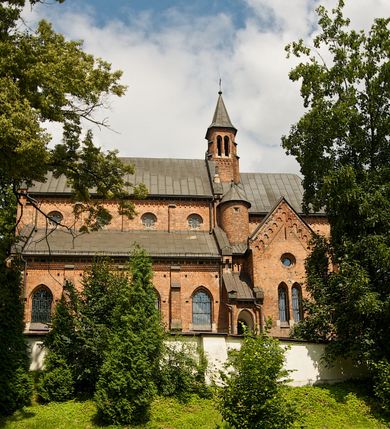 Zdjęcie nr 8: Murowana z cegły, orientowana, trzynawowa bazylika emporowa z prezbiterium zamkniętym trójbocznie. Do jednej czwartej wysokości murów lico kamienne, całość obiega cokół. Fasada dwukondygnacyjna, trójosiowa; oś środkowa wysunięta przed lico muru. Podziały pionowe tworzą dwuuskokowe przypory, poziome gzyms w połowie wysokości osi środkowej. Na osi portal ostrołukowy, uskokowy, flankowany filarami wspartymi na wysokich cokołach. W filarach fragmenty laski. Powyżej wsporniki podtrzymujące wąską archiwoltę otoczoną fryzem arkadowym. Nad otworem drzwiowym tympanon o zarysie łuku ostrego. W zwieńczeniu trójkątny przyczółek, którego ramiona spływają na konsolki oparte na filarach; całość wieńczy krzyż. Ponad portalem dwa okna w uskokowym obramieniu zakończonym łukiem ostrym. Ponad nimi okrągłe okno, wyżej kamienny kartusz z herbem fundatorki. Fasadę wieńczy ząbkowanie i fryz arkadowy. W skrajnych osiach okna ostrołukowe. W dolnym, lewym rogu osi środkowej data: MCMV. Podziały ścian nawy bocznej stanowią trójskokowe przypory; pomiędzy nimi okna ostrołukowe w uskokowych obramieniach. Ponad oknami ząbkowanie, profilowany architraw, fryz i gzyms wsparty na kroksztynach. W partii nawy głównej podział ścian tworzą małe przypory, pomiędzy którymi znajdują się okrągłe okna, ponad nimi fryz arkadowy. W zwieńczeniu kroksztyny. W ścianach zakrystii dwa wąskie, ostrołukowe okna i jedno okrągłe w profilowanych obramieniach. W trójkątnym zwieńczeniu fryz arkadowy ujęty w dwa pasy ząbkowania. Przy zachodniej ścianie południowej zakrystii znajduje się boczne wejście otwarte dwoma ostrołukowymi arkadami, wspartymi na filarze. W górnej partii ozdobione fryzem arkadowym, ząbkowaniem i kroksztynami. Pomiędzy nawą boczną a południową zakrystią okrągła wieżyczka z dwoma kwadratowymi otworami okiennymi. Strona północna analogiczna do południowej, oprócz pomieszczenia między nawą a zakrystią i portalu w pomieszczeniu przy kruchcie. Pomieszczenie z wejściem pomocniczym od strony zachodniej Od północy wąskie okno zamknięte łukiem półkolistym, w narożach ryzality zwieńczone konsolkami z fryzem arkadowym i gzymsem pomiędzy. Portal kamienny, ustawiony na czterech stopniach, ostrołukowy, zwieńczony trójkątnym przyczółkiem z ramionami spływającymi na profilowane konsole. Prezbiterium opięte czterema przyporami dwuuskokowymi. W ścianie wschodniej płycina zakończona łukiem ostrym. W zwieńczeniu fryz arkadowy i gzyms wsparty na kroksztynach. Pomiędzy nawą główną, a prezbiterium wieżyczka na sygnaturkę na planie kwadratu ze ściętymi narożami, przy których znajdują się dwuuskokowe przypory. We wszystkich ścianach wieżyczki po dwa okna ostrołukowe z parapetem, pod nim fryz arkadowy. Ściany wieńczy pas kostkowania. Nawa główna, część prezbiterium i zakrystie przykrywa dach dwuspadowy, z zakończeniu prezbiterium dach powtarza kształt prezbiterium. Nawy boczne nakryte dachem pulpitowym, wieżyczka dachem stożkowym, wieżyczka na sygnaturkę ostrosłupowym ze ściętymi krawędziami. Wszystkie dachy blaszane.Najcenniejszy wyposażenie wnętrza stanowią trzy późnobarokowe ołtarze z 1710 roku (w głównym obraz św. Marii Magdaleny z początku XVIII wieku w sukience z 1709 roku,) ambona z 1711 oraz chrzcielnica czarnomarmurowa z 1751 roku.
