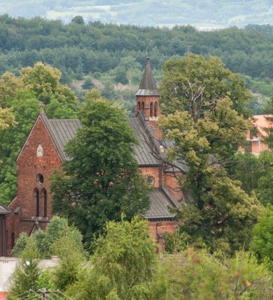 Zdjęcie nr 2: Murowana z cegły, orientowana, trzynawowa bazylika emporowa z prezbiterium zamkniętym trójbocznie. Do jednej czwartej wysokości murów lico kamienne, całość obiega cokół. Fasada dwukondygnacyjna, trójosiowa; oś środkowa wysunięta przed lico muru. Podziały pionowe tworzą dwuuskokowe przypory, poziome gzyms w połowie wysokości osi środkowej. Na osi portal ostrołukowy, uskokowy, flankowany filarami wspartymi na wysokich cokołach. W filarach fragmenty laski. Powyżej wsporniki podtrzymujące wąską archiwoltę otoczoną fryzem arkadowym. Nad otworem drzwiowym tympanon o zarysie łuku ostrego. W zwieńczeniu trójkątny przyczółek, którego ramiona spływają na konsolki oparte na filarach; całość wieńczy krzyż. Ponad portalem dwa okna w uskokowym obramieniu zakończonym łukiem ostrym. Ponad nimi okrągłe okno, wyżej kamienny kartusz z herbem fundatorki. Fasadę wieńczy ząbkowanie i fryz arkadowy. W skrajnych osiach okna ostrołukowe. W dolnym, lewym rogu osi środkowej data: MCMV. Podziały ścian nawy bocznej stanowią trójskokowe przypory; pomiędzy nimi okna ostrołukowe w uskokowych obramieniach. Ponad oknami ząbkowanie, profilowany architraw, fryz i gzyms wsparty na kroksztynach. W partii nawy głównej podział ścian tworzą małe przypory, pomiędzy którymi znajdują się okrągłe okna, ponad nimi fryz arkadowy. W zwieńczeniu kroksztyny. W ścianach zakrystii dwa wąskie, ostrołukowe okna i jedno okrągłe w profilowanych obramieniach. W trójkątnym zwieńczeniu fryz arkadowy ujęty w dwa pasy ząbkowania. Przy zachodniej ścianie południowej zakrystii znajduje się boczne wejście otwarte dwoma ostrołukowymi arkadami, wspartymi na filarze. W górnej partii ozdobione fryzem arkadowym, ząbkowaniem i kroksztynami. Pomiędzy nawą boczną a południową zakrystią okrągła wieżyczka z dwoma kwadratowymi otworami okiennymi. Strona północna analogiczna do południowej, oprócz pomieszczenia między nawą a zakrystią i portalu w pomieszczeniu przy kruchcie. Pomieszczenie z wejściem pomocniczym od strony zachodniej Od północy wąskie okno zamknięte łukiem półkolistym, w narożach ryzality zwieńczone konsolkami z fryzem arkadowym i gzymsem pomiędzy. Portal kamienny, ustawiony na czterech stopniach, ostrołukowy, zwieńczony trójkątnym przyczółkiem z ramionami spływającymi na profilowane konsole. Prezbiterium opięte czterema przyporami dwuuskokowymi. W ścianie wschodniej płycina zakończona łukiem ostrym. W zwieńczeniu fryz arkadowy i gzyms wsparty na kroksztynach. Pomiędzy nawą główną, a prezbiterium wieżyczka na sygnaturkę na planie kwadratu ze ściętymi narożami, przy których znajdują się dwuuskokowe przypory. We wszystkich ścianach wieżyczki po dwa okna ostrołukowe z parapetem, pod nim fryz arkadowy. Ściany wieńczy pas kostkowania. Nawa główna, część prezbiterium i zakrystie przykrywa dach dwuspadowy, z zakończeniu prezbiterium dach powtarza kształt prezbiterium. Nawy boczne nakryte dachem pulpitowym, wieżyczka dachem stożkowym, wieżyczka na sygnaturkę ostrosłupowym ze ściętymi krawędziami. Wszystkie dachy blaszane.Najcenniejszy wyposażenie wnętrza stanowią trzy późnobarokowe ołtarze z 1710 roku (w głównym obraz św. Marii Magdaleny z początku XVIII wieku w sukience z 1709 roku,) ambona z 1711 oraz chrzcielnica czarnomarmurowa z 1751 roku.