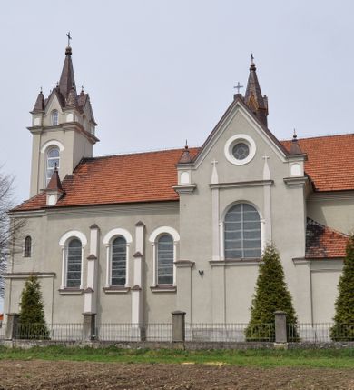 Zdjęcie nr 13: Kościół na planie krzyża łacińskiego, jednonawowy, pięcioprzęsłowy, z transeptem i jednoprzęsłowym prezbiterium zakończonym wielobocznie. Ramiona transeptu jednoprzęsłowe, o wysokości nawy, zamknięte prostymi ścianami. W narożnikach pomiędzy prezbiterium i ramionami transeptu dwa prostokątne aneksy mieszczące zakrystię i skarbiec. Prezbiterium i ramiona transeptu oddzielone od nawy wydatnymi półfilarami przechodzącymi bezpośrednio w gurty sklepienne. Prezbiterium od absydy oddziela arkada tęczowa wsparta na dostawionych do węgarów kolumnach kompozytowych. Sklepienie nad skrzyżowaniem naw krzyżowe, nad pozostałymi przęsłami nawy kolebkowe o przekroju koszowym, nad ramionami transeptu krzyżowe (ostrołukowe), w absydzie ćwierćsferyczne z lunetami. Otwory okienne prostokątne, zamknięte półkoliście, rozglifione do wewnątrz; trzy pary w nawie, dwa na ścianach zamykających ramiona transeptu. Ponad oknami w transepcie dodatkowo po jednym okrągłym oknie wypełnionym rozetą. W prezbiterium okna w kształcie wydłużonego prostokąta o smukłych proporcjach zamkniętego półkoliście, pomiędzy nimi para regularnie rozmieszczonych okien owalnych.  W zachodnim przęśle nawy murowany trójprzęsłowy chór muzyczny wsparty na parze ośmiobocznych filarów z cokołami, a pod ścianami na parze półfilarów. Balustrada o prostej dekoracji płycinowej. Podniebie chóru podzielone belkami na trzy kasetony, pośrodku których kwadratowe płyciny. Fasada kościoła dwukondygnacyjna, trójosiowa przechodząca w czworoboczną wieżę. Ściany rozczłonkowane lizenami, kondygnacje oddzielone profilowanym gzymsem. W części środkowej wejście zamknięte łukiem półkolistym, z dwuspadowym drewnianym daszkiem, wyżej prostokątne okno zamknięte półkoliście. W polach bocznych mniejsze, prostokątne okna zamknięte półkoliście. Wieża o narożach ujętych lizenami, podtrzymującymi gzyms, nakryta ozdobnym zwieńczeniem z czterema wieżyczkami w narożach, pomiędzy którymi trójkątne szczyciki nad oknami i ostrosłupowy hełm zakończony krzyżem. Ściany boczne nawy i transeptu ujęte uskokowymi przyporami. Ściany zamykające ramiona transeptu podzielone na dwie strefy, z których dolna ujęta lizenami, górna wypełniona oknem w ozdobnym obramieniu. Dachy dwuspadowe, kryte dachówką. Na skrzyżowaniu naw wieloboczna, drewniana wieżyczka na sygnaturkę nakryta ostrosłupowym hełmem pokrytym blachą.

