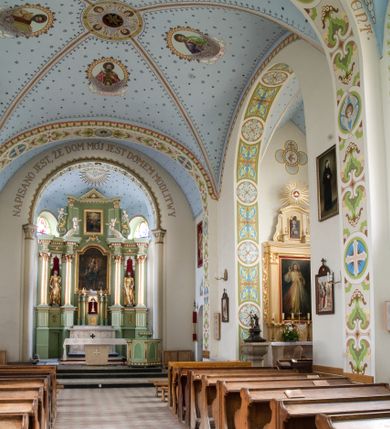 Zdjęcie nr 20: Kościół na planie krzyża łacińskiego, jednonawowy, pięcioprzęsłowy, z transeptem i jednoprzęsłowym prezbiterium zakończonym wielobocznie. Ramiona transeptu jednoprzęsłowe, o wysokości nawy, zamknięte prostymi ścianami. W narożnikach pomiędzy prezbiterium i ramionami transeptu dwa prostokątne aneksy mieszczące zakrystię i skarbiec. Prezbiterium i ramiona transeptu oddzielone od nawy wydatnymi półfilarami przechodzącymi bezpośrednio w gurty sklepienne. Prezbiterium od absydy oddziela arkada tęczowa wsparta na dostawionych do węgarów kolumnach kompozytowych. Sklepienie nad skrzyżowaniem naw krzyżowe, nad pozostałymi przęsłami nawy kolebkowe o przekroju koszowym, nad ramionami transeptu krzyżowe (ostrołukowe), w absydzie ćwierćsferyczne z lunetami. Otwory okienne prostokątne, zamknięte półkoliście, rozglifione do wewnątrz; trzy pary w nawie, dwa na ścianach zamykających ramiona transeptu. Ponad oknami w transepcie dodatkowo po jednym okrągłym oknie wypełnionym rozetą. W prezbiterium okna w kształcie wydłużonego prostokąta o smukłych proporcjach zamkniętego półkoliście, pomiędzy nimi para regularnie rozmieszczonych okien owalnych.  W zachodnim przęśle nawy murowany trójprzęsłowy chór muzyczny wsparty na parze ośmiobocznych filarów z cokołami, a pod ścianami na parze półfilarów. Balustrada o prostej dekoracji płycinowej. Podniebie chóru podzielone belkami na trzy kasetony, pośrodku których kwadratowe płyciny. Fasada kościoła dwukondygnacyjna, trójosiowa przechodząca w czworoboczną wieżę. Ściany rozczłonkowane lizenami, kondygnacje oddzielone profilowanym gzymsem. W części środkowej wejście zamknięte łukiem półkolistym, z dwuspadowym drewnianym daszkiem, wyżej prostokątne okno zamknięte półkoliście. W polach bocznych mniejsze, prostokątne okna zamknięte półkoliście. Wieża o narożach ujętych lizenami, podtrzymującymi gzyms, nakryta ozdobnym zwieńczeniem z czterema wieżyczkami w narożach, pomiędzy którymi trójkątne szczyciki nad oknami i ostrosłupowy hełm zakończony krzyżem. Ściany boczne nawy i transeptu ujęte uskokowymi przyporami. Ściany zamykające ramiona transeptu podzielone na dwie strefy, z których dolna ujęta lizenami, górna wypełniona oknem w ozdobnym obramieniu. Dachy dwuspadowe, kryte dachówką. Na skrzyżowaniu naw wieloboczna, drewniana wieżyczka na sygnaturkę nakryta ostrosłupowym hełmem pokrytym blachą.

