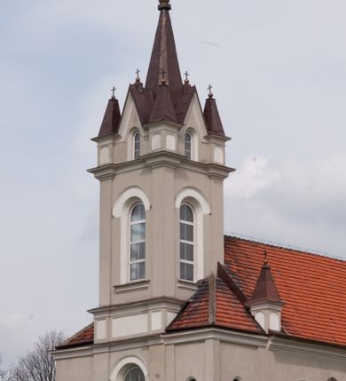 Zdjęcie nr 8: Kościół na planie krzyża łacińskiego, jednonawowy, pięcioprzęsłowy, z transeptem i jednoprzęsłowym prezbiterium zakończonym wielobocznie. Ramiona transeptu jednoprzęsłowe, o wysokości nawy, zamknięte prostymi ścianami. W narożnikach pomiędzy prezbiterium i ramionami transeptu dwa prostokątne aneksy mieszczące zakrystię i skarbiec. Prezbiterium i ramiona transeptu oddzielone od nawy wydatnymi półfilarami przechodzącymi bezpośrednio w gurty sklepienne. Prezbiterium od absydy oddziela arkada tęczowa wsparta na dostawionych do węgarów kolumnach kompozytowych. Sklepienie nad skrzyżowaniem naw krzyżowe, nad pozostałymi przęsłami nawy kolebkowe o przekroju koszowym, nad ramionami transeptu krzyżowe (ostrołukowe), w absydzie ćwierćsferyczne z lunetami. Otwory okienne prostokątne, zamknięte półkoliście, rozglifione do wewnątrz; trzy pary w nawie, dwa na ścianach zamykających ramiona transeptu. Ponad oknami w transepcie dodatkowo po jednym okrągłym oknie wypełnionym rozetą. W prezbiterium okna w kształcie wydłużonego prostokąta o smukłych proporcjach zamkniętego półkoliście, pomiędzy nimi para regularnie rozmieszczonych okien owalnych.  W zachodnim przęśle nawy murowany trójprzęsłowy chór muzyczny wsparty na parze ośmiobocznych filarów z cokołami, a pod ścianami na parze półfilarów. Balustrada o prostej dekoracji płycinowej. Podniebie chóru podzielone belkami na trzy kasetony, pośrodku których kwadratowe płyciny. Fasada kościoła dwukondygnacyjna, trójosiowa przechodząca w czworoboczną wieżę. Ściany rozczłonkowane lizenami, kondygnacje oddzielone profilowanym gzymsem. W części środkowej wejście zamknięte łukiem półkolistym, z dwuspadowym drewnianym daszkiem, wyżej prostokątne okno zamknięte półkoliście. W polach bocznych mniejsze, prostokątne okna zamknięte półkoliście. Wieża o narożach ujętych lizenami, podtrzymującymi gzyms, nakryta ozdobnym zwieńczeniem z czterema wieżyczkami w narożach, pomiędzy którymi trójkątne szczyciki nad oknami i ostrosłupowy hełm zakończony krzyżem. Ściany boczne nawy i transeptu ujęte uskokowymi przyporami. Ściany zamykające ramiona transeptu podzielone na dwie strefy, z których dolna ujęta lizenami, górna wypełniona oknem w ozdobnym obramieniu. Dachy dwuspadowe, kryte dachówką. Na skrzyżowaniu naw wieloboczna, drewniana wieżyczka na sygnaturkę nakryta ostrosłupowym hełmem pokrytym blachą.

