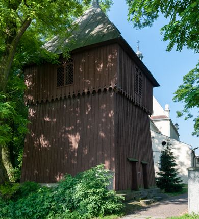 Zdjęcie nr 5: Budynek orientowany, jednonawowy. Prostokątna nawa jest szersza i znacznie wyższa, oddzielona od prezbiterium za pomocą ściany tarczowej z ostrołukową arkadą tęczową. Przy prezbiterium od północy zakrystia na planie prostokąta i taki sam skarbczyk, od południa niewielka, prostokątna kruchta. Przy nawie od południa podłużna kaplica Matki Boskiej Szkaplerznej (1741) z kwadratową kruchtą od zachodu; od północy kaplica Matki Boskiej Bolesnej na planie półokręgu z obejściem (1919-1932, projektu Bogdana Tretera). Prezbiterium sklepione krzyżowo-żebrowo, korpus sześciodzielnie, z gurtami. 
Okna nawy i kaplicy południowej ostrołukowe; w zwieńczeniu zakrystii jedno okno okrągłe; w kaplicy południowej okna zamknięte półkoliście, w kopule lukarny z eliptycznymi otworami okiennymi. 
Główne wejście od zachodu, ostrołukowe, drugie przez kruchtę od północy, w kształcie stojącego prostokąta. Portal z prezbiterium do zakrystii kamienny, profilowany zamknięty ściętym trójliściem (XV/XVI w.); portal z kruchty północnej do kaplicy kamienny, ostrołukowy, profilowany i fazowany, nad nim późnogotycka tarcza z herbem Nieczuja. Nad zewnętrznym, ostrołukowym portalem do kruchty północnej herb Korab i insygnia biskupa Jakuba Zadzika, pochodzące prawdopodobnie z dawnej bramy przejazdowej obok katedry w Kielcach. 
Na zewnątrz budynek opięty przyporami o zmiennym profilu. Elewacje, z wyjątkiem wschodniej ściany prezbiterium, tynkowane. Fasada zamknięta wysokim, trójkątnym szczytem, trójosiowa. W osi środkowej kamienny, ostrołukowy portal. W osiach bocznych ostrołukowe okna. Narożniki ujęte modelowanymi w tynku lizenami oraz przyporami. Powyżej na ich osiach prostopadłościenne sterczyny zwieńczone krzyżami. Elewacja wschodnia o analogicznym układzie, ceglana, nietynkowana, ujęta skośnie ustawionymi przyporami, jednoosiowa. W osi szeroka, jednouskokowa przypora z kamienną płyciną mieszczącą krucyfiks w dolnej części i analogiczną, mniejszą z kamienną figurą św. Piotra na tle okna powyżej. Na ścianie szczytowej cegły ułożone w jodełkę, w górnej części ostrołukowa, uskokowa płycina. Na zwieńczeniu wyryty napis „RENO/VATUM / A(NNO) D(OMINI)/ 1928”.  Elewacja północna z dobudowanymi na całej długości zakrystią, skarbczykiem i kaplicą. Elewacja południowa tynkowana, w części prezbiterium dwuosiowa; w narożniku pomiędzy prezbiterium a nawą niewielka kruchta. Do korpusu dobudowana kaplica – z tynkowanymi elewacjami o osiach podkreślonych lizenami, zróżnicowanymi kolorystycznie. Dach nad korpusem nawowym i prezbiterium dwuspadowy, nad zakrystią i skarbczykiem dachy pulpitowe –  kryte dachówką. Kaplica południowa nakryta kopułą z lunetami i latarnią – kryta blachą. Wieżyczka na sygnaturkę o formach barokowych z latarnią.