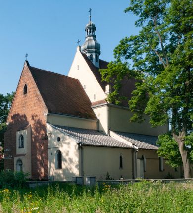 Zdjęcie nr 1: Budynek orientowany, jednonawowy. Prostokątna nawa jest szersza i znacznie wyższa, oddzielona od prezbiterium za pomocą ściany tarczowej z ostrołukową arkadą tęczową. Przy prezbiterium od północy zakrystia na planie prostokąta i taki sam skarbczyk, od południa niewielka, prostokątna kruchta. Przy nawie od południa podłużna kaplica Matki Boskiej Szkaplerznej (1741) z kwadratową kruchtą od zachodu; od północy kaplica Matki Boskiej Bolesnej na planie półokręgu z obejściem (1919-1932, projektu Bogdana Tretera). Prezbiterium sklepione krzyżowo-żebrowo, korpus sześciodzielnie, z gurtami. 
Okna nawy i kaplicy południowej ostrołukowe; w zwieńczeniu zakrystii jedno okno okrągłe; w kaplicy południowej okna zamknięte półkoliście, w kopule lukarny z eliptycznymi otworami okiennymi. 
Główne wejście od zachodu, ostrołukowe, drugie przez kruchtę od północy, w kształcie stojącego prostokąta. Portal z prezbiterium do zakrystii kamienny, profilowany zamknięty ściętym trójliściem (XV/XVI w.); portal z kruchty północnej do kaplicy kamienny, ostrołukowy, profilowany i fazowany, nad nim późnogotycka tarcza z herbem Nieczuja. Nad zewnętrznym, ostrołukowym portalem do kruchty północnej herb Korab i insygnia biskupa Jakuba Zadzika, pochodzące prawdopodobnie z dawnej bramy przejazdowej obok katedry w Kielcach. 
Na zewnątrz budynek opięty przyporami o zmiennym profilu. Elewacje, z wyjątkiem wschodniej ściany prezbiterium, tynkowane. Fasada zamknięta wysokim, trójkątnym szczytem, trójosiowa. W osi środkowej kamienny, ostrołukowy portal. W osiach bocznych ostrołukowe okna. Narożniki ujęte modelowanymi w tynku lizenami oraz przyporami. Powyżej na ich osiach prostopadłościenne sterczyny zwieńczone krzyżami. Elewacja wschodnia o analogicznym układzie, ceglana, nietynkowana, ujęta skośnie ustawionymi przyporami, jednoosiowa. W osi szeroka, jednouskokowa przypora z kamienną płyciną mieszczącą krucyfiks w dolnej części i analogiczną, mniejszą z kamienną figurą św. Piotra na tle okna powyżej. Na ścianie szczytowej cegły ułożone w jodełkę, w górnej części ostrołukowa, uskokowa płycina. Na zwieńczeniu wyryty napis „RENO/VATUM / A(NNO) D(OMINI)/ 1928”.  Elewacja północna z dobudowanymi na całej długości zakrystią, skarbczykiem i kaplicą. Elewacja południowa tynkowana, w części prezbiterium dwuosiowa; w narożniku pomiędzy prezbiterium a nawą niewielka kruchta. Do korpusu dobudowana kaplica – z tynkowanymi elewacjami o osiach podkreślonych lizenami, zróżnicowanymi kolorystycznie. Dach nad korpusem nawowym i prezbiterium dwuspadowy, nad zakrystią i skarbczykiem dachy pulpitowe –  kryte dachówką. Kaplica południowa nakryta kopułą z lunetami i latarnią – kryta blachą. Wieżyczka na sygnaturkę o formach barokowych z latarnią.