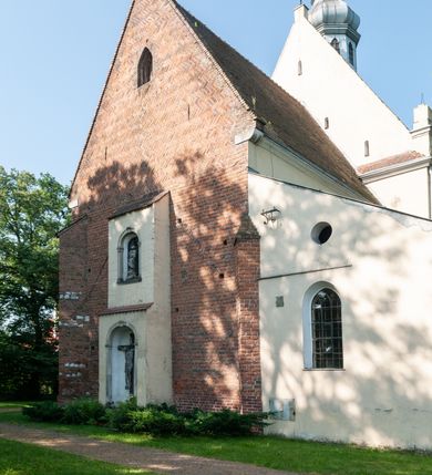 Zdjęcie nr 4: Budynek orientowany, jednonawowy. Prostokątna nawa jest szersza i znacznie wyższa, oddzielona od prezbiterium za pomocą ściany tarczowej z ostrołukową arkadą tęczową. Przy prezbiterium od północy zakrystia na planie prostokąta i taki sam skarbczyk, od południa niewielka, prostokątna kruchta. Przy nawie od południa podłużna kaplica Matki Boskiej Szkaplerznej (1741) z kwadratową kruchtą od zachodu; od północy kaplica Matki Boskiej Bolesnej na planie półokręgu z obejściem (1919-1932, projektu Bogdana Tretera). Prezbiterium sklepione krzyżowo-żebrowo, korpus sześciodzielnie, z gurtami. 
Okna nawy i kaplicy południowej ostrołukowe; w zwieńczeniu zakrystii jedno okno okrągłe; w kaplicy południowej okna zamknięte półkoliście, w kopule lukarny z eliptycznymi otworami okiennymi. 
Główne wejście od zachodu, ostrołukowe, drugie przez kruchtę od północy, w kształcie stojącego prostokąta. Portal z prezbiterium do zakrystii kamienny, profilowany zamknięty ściętym trójliściem (XV/XVI w.); portal z kruchty północnej do kaplicy kamienny, ostrołukowy, profilowany i fazowany, nad nim późnogotycka tarcza z herbem Nieczuja. Nad zewnętrznym, ostrołukowym portalem do kruchty północnej herb Korab i insygnia biskupa Jakuba Zadzika, pochodzące prawdopodobnie z dawnej bramy przejazdowej obok katedry w Kielcach. 
Na zewnątrz budynek opięty przyporami o zmiennym profilu. Elewacje, z wyjątkiem wschodniej ściany prezbiterium, tynkowane. Fasada zamknięta wysokim, trójkątnym szczytem, trójosiowa. W osi środkowej kamienny, ostrołukowy portal. W osiach bocznych ostrołukowe okna. Narożniki ujęte modelowanymi w tynku lizenami oraz przyporami. Powyżej na ich osiach prostopadłościenne sterczyny zwieńczone krzyżami. Elewacja wschodnia o analogicznym układzie, ceglana, nietynkowana, ujęta skośnie ustawionymi przyporami, jednoosiowa. W osi szeroka, jednouskokowa przypora z kamienną płyciną mieszczącą krucyfiks w dolnej części i analogiczną, mniejszą z kamienną figurą św. Piotra na tle okna powyżej. Na ścianie szczytowej cegły ułożone w jodełkę, w górnej części ostrołukowa, uskokowa płycina. Na zwieńczeniu wyryty napis „RENO/VATUM / A(NNO) D(OMINI)/ 1928”.  Elewacja północna z dobudowanymi na całej długości zakrystią, skarbczykiem i kaplicą. Elewacja południowa tynkowana, w części prezbiterium dwuosiowa; w narożniku pomiędzy prezbiterium a nawą niewielka kruchta. Do korpusu dobudowana kaplica – z tynkowanymi elewacjami o osiach podkreślonych lizenami, zróżnicowanymi kolorystycznie. Dach nad korpusem nawowym i prezbiterium dwuspadowy, nad zakrystią i skarbczykiem dachy pulpitowe –  kryte dachówką. Kaplica południowa nakryta kopułą z lunetami i latarnią – kryta blachą. Wieżyczka na sygnaturkę o formach barokowych z latarnią.