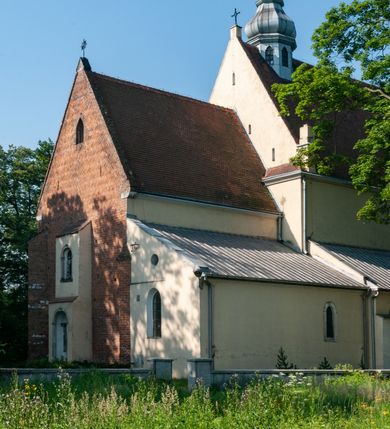 Zdjęcie nr 6: Budynek orientowany, jednonawowy. Prostokątna nawa jest szersza i znacznie wyższa, oddzielona od prezbiterium za pomocą ściany tarczowej z ostrołukową arkadą tęczową. Przy prezbiterium od północy zakrystia na planie prostokąta i taki sam skarbczyk, od południa niewielka, prostokątna kruchta. Przy nawie od południa podłużna kaplica Matki Boskiej Szkaplerznej (1741) z kwadratową kruchtą od zachodu; od północy kaplica Matki Boskiej Bolesnej na planie półokręgu z obejściem (1919-1932, projektu Bogdana Tretera). Prezbiterium sklepione krzyżowo-żebrowo, korpus sześciodzielnie, z gurtami. 
Okna nawy i kaplicy południowej ostrołukowe; w zwieńczeniu zakrystii jedno okno okrągłe; w kaplicy południowej okna zamknięte półkoliście, w kopule lukarny z eliptycznymi otworami okiennymi. 
Główne wejście od zachodu, ostrołukowe, drugie przez kruchtę od północy, w kształcie stojącego prostokąta. Portal z prezbiterium do zakrystii kamienny, profilowany zamknięty ściętym trójliściem (XV/XVI w.); portal z kruchty północnej do kaplicy kamienny, ostrołukowy, profilowany i fazowany, nad nim późnogotycka tarcza z herbem Nieczuja. Nad zewnętrznym, ostrołukowym portalem do kruchty północnej herb Korab i insygnia biskupa Jakuba Zadzika, pochodzące prawdopodobnie z dawnej bramy przejazdowej obok katedry w Kielcach. 
Na zewnątrz budynek opięty przyporami o zmiennym profilu. Elewacje, z wyjątkiem wschodniej ściany prezbiterium, tynkowane. Fasada zamknięta wysokim, trójkątnym szczytem, trójosiowa. W osi środkowej kamienny, ostrołukowy portal. W osiach bocznych ostrołukowe okna. Narożniki ujęte modelowanymi w tynku lizenami oraz przyporami. Powyżej na ich osiach prostopadłościenne sterczyny zwieńczone krzyżami. Elewacja wschodnia o analogicznym układzie, ceglana, nietynkowana, ujęta skośnie ustawionymi przyporami, jednoosiowa. W osi szeroka, jednouskokowa przypora z kamienną płyciną mieszczącą krucyfiks w dolnej części i analogiczną, mniejszą z kamienną figurą św. Piotra na tle okna powyżej. Na ścianie szczytowej cegły ułożone w jodełkę, w górnej części ostrołukowa, uskokowa płycina. Na zwieńczeniu wyryty napis „RENO/VATUM / A(NNO) D(OMINI)/ 1928”.  Elewacja północna z dobudowanymi na całej długości zakrystią, skarbczykiem i kaplicą. Elewacja południowa tynkowana, w części prezbiterium dwuosiowa; w narożniku pomiędzy prezbiterium a nawą niewielka kruchta. Do korpusu dobudowana kaplica – z tynkowanymi elewacjami o osiach podkreślonych lizenami, zróżnicowanymi kolorystycznie. Dach nad korpusem nawowym i prezbiterium dwuspadowy, nad zakrystią i skarbczykiem dachy pulpitowe –  kryte dachówką. Kaplica południowa nakryta kopułą z lunetami i latarnią – kryta blachą. Wieżyczka na sygnaturkę o formach barokowych z latarnią.