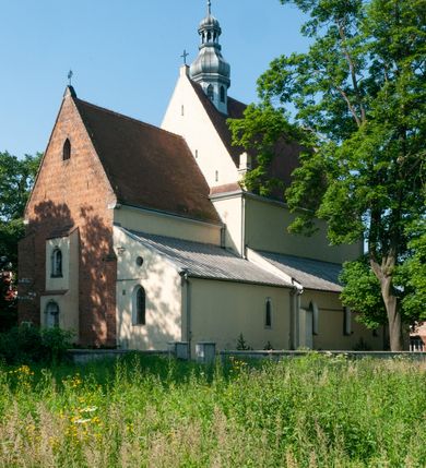 Zdjęcie nr 2: Budynek orientowany, jednonawowy. Prostokątna nawa jest szersza i znacznie wyższa, oddzielona od prezbiterium za pomocą ściany tarczowej z ostrołukową arkadą tęczową. Przy prezbiterium od północy zakrystia na planie prostokąta i taki sam skarbczyk, od południa niewielka, prostokątna kruchta. Przy nawie od południa podłużna kaplica Matki Boskiej Szkaplerznej (1741) z kwadratową kruchtą od zachodu; od północy kaplica Matki Boskiej Bolesnej na planie półokręgu z obejściem (1919-1932, projektu Bogdana Tretera). Prezbiterium sklepione krzyżowo-żebrowo, korpus sześciodzielnie, z gurtami. 
Okna nawy i kaplicy południowej ostrołukowe; w zwieńczeniu zakrystii jedno okno okrągłe; w kaplicy południowej okna zamknięte półkoliście, w kopule lukarny z eliptycznymi otworami okiennymi. 
Główne wejście od zachodu, ostrołukowe, drugie przez kruchtę od północy, w kształcie stojącego prostokąta. Portal z prezbiterium do zakrystii kamienny, profilowany zamknięty ściętym trójliściem (XV/XVI w.); portal z kruchty północnej do kaplicy kamienny, ostrołukowy, profilowany i fazowany, nad nim późnogotycka tarcza z herbem Nieczuja. Nad zewnętrznym, ostrołukowym portalem do kruchty północnej herb Korab i insygnia biskupa Jakuba Zadzika, pochodzące prawdopodobnie z dawnej bramy przejazdowej obok katedry w Kielcach. 
Na zewnątrz budynek opięty przyporami o zmiennym profilu. Elewacje, z wyjątkiem wschodniej ściany prezbiterium, tynkowane. Fasada zamknięta wysokim, trójkątnym szczytem, trójosiowa. W osi środkowej kamienny, ostrołukowy portal. W osiach bocznych ostrołukowe okna. Narożniki ujęte modelowanymi w tynku lizenami oraz przyporami. Powyżej na ich osiach prostopadłościenne sterczyny zwieńczone krzyżami. Elewacja wschodnia o analogicznym układzie, ceglana, nietynkowana, ujęta skośnie ustawionymi przyporami, jednoosiowa. W osi szeroka, jednouskokowa przypora z kamienną płyciną mieszczącą krucyfiks w dolnej części i analogiczną, mniejszą z kamienną figurą św. Piotra na tle okna powyżej. Na ścianie szczytowej cegły ułożone w jodełkę, w górnej części ostrołukowa, uskokowa płycina. Na zwieńczeniu wyryty napis „RENO/VATUM / A(NNO) D(OMINI)/ 1928”.  Elewacja północna z dobudowanymi na całej długości zakrystią, skarbczykiem i kaplicą. Elewacja południowa tynkowana, w części prezbiterium dwuosiowa; w narożniku pomiędzy prezbiterium a nawą niewielka kruchta. Do korpusu dobudowana kaplica – z tynkowanymi elewacjami o osiach podkreślonych lizenami, zróżnicowanymi kolorystycznie. Dach nad korpusem nawowym i prezbiterium dwuspadowy, nad zakrystią i skarbczykiem dachy pulpitowe –  kryte dachówką. Kaplica południowa nakryta kopułą z lunetami i latarnią – kryta blachą. Wieżyczka na sygnaturkę o formach barokowych z latarnią.
