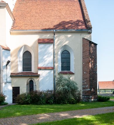 Zdjęcie nr 10: Budynek orientowany, jednonawowy. Prostokątna nawa jest szersza i znacznie wyższa, oddzielona od prezbiterium za pomocą ściany tarczowej z ostrołukową arkadą tęczową. Przy prezbiterium od północy zakrystia na planie prostokąta i taki sam skarbczyk, od południa niewielka, prostokątna kruchta. Przy nawie od południa podłużna kaplica Matki Boskiej Szkaplerznej (1741) z kwadratową kruchtą od zachodu; od północy kaplica Matki Boskiej Bolesnej na planie półokręgu z obejściem (1919-1932, projektu Bogdana Tretera). Prezbiterium sklepione krzyżowo-żebrowo, korpus sześciodzielnie, z gurtami. 
Okna nawy i kaplicy południowej ostrołukowe; w zwieńczeniu zakrystii jedno okno okrągłe; w kaplicy południowej okna zamknięte półkoliście, w kopule lukarny z eliptycznymi otworami okiennymi. 
Główne wejście od zachodu, ostrołukowe, drugie przez kruchtę od północy, w kształcie stojącego prostokąta. Portal z prezbiterium do zakrystii kamienny, profilowany zamknięty ściętym trójliściem (XV/XVI w.); portal z kruchty północnej do kaplicy kamienny, ostrołukowy, profilowany i fazowany, nad nim późnogotycka tarcza z herbem Nieczuja. Nad zewnętrznym, ostrołukowym portalem do kruchty północnej herb Korab i insygnia biskupa Jakuba Zadzika, pochodzące prawdopodobnie z dawnej bramy przejazdowej obok katedry w Kielcach. 
Na zewnątrz budynek opięty przyporami o zmiennym profilu. Elewacje, z wyjątkiem wschodniej ściany prezbiterium, tynkowane. Fasada zamknięta wysokim, trójkątnym szczytem, trójosiowa. W osi środkowej kamienny, ostrołukowy portal. W osiach bocznych ostrołukowe okna. Narożniki ujęte modelowanymi w tynku lizenami oraz przyporami. Powyżej na ich osiach prostopadłościenne sterczyny zwieńczone krzyżami. Elewacja wschodnia o analogicznym układzie, ceglana, nietynkowana, ujęta skośnie ustawionymi przyporami, jednoosiowa. W osi szeroka, jednouskokowa przypora z kamienną płyciną mieszczącą krucyfiks w dolnej części i analogiczną, mniejszą z kamienną figurą św. Piotra na tle okna powyżej. Na ścianie szczytowej cegły ułożone w jodełkę, w górnej części ostrołukowa, uskokowa płycina. Na zwieńczeniu wyryty napis „RENO/VATUM / A(NNO) D(OMINI)/ 1928”.  Elewacja północna z dobudowanymi na całej długości zakrystią, skarbczykiem i kaplicą. Elewacja południowa tynkowana, w części prezbiterium dwuosiowa; w narożniku pomiędzy prezbiterium a nawą niewielka kruchta. Do korpusu dobudowana kaplica – z tynkowanymi elewacjami o osiach podkreślonych lizenami, zróżnicowanymi kolorystycznie. Dach nad korpusem nawowym i prezbiterium dwuspadowy, nad zakrystią i skarbczykiem dachy pulpitowe –  kryte dachówką. Kaplica południowa nakryta kopułą z lunetami i latarnią – kryta blachą. Wieżyczka na sygnaturkę o formach barokowych z latarnią.