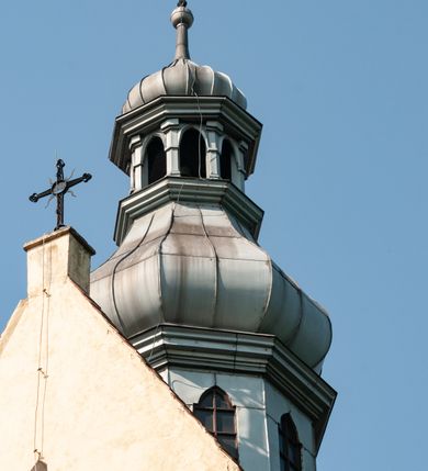 Zdjęcie nr 9: Budynek orientowany, jednonawowy. Prostokątna nawa jest szersza i znacznie wyższa, oddzielona od prezbiterium za pomocą ściany tarczowej z ostrołukową arkadą tęczową. Przy prezbiterium od północy zakrystia na planie prostokąta i taki sam skarbczyk, od południa niewielka, prostokątna kruchta. Przy nawie od południa podłużna kaplica Matki Boskiej Szkaplerznej (1741) z kwadratową kruchtą od zachodu; od północy kaplica Matki Boskiej Bolesnej na planie półokręgu z obejściem (1919-1932, projektu Bogdana Tretera). Prezbiterium sklepione krzyżowo-żebrowo, korpus sześciodzielnie, z gurtami. 
Okna nawy i kaplicy południowej ostrołukowe; w zwieńczeniu zakrystii jedno okno okrągłe; w kaplicy południowej okna zamknięte półkoliście, w kopule lukarny z eliptycznymi otworami okiennymi. 
Główne wejście od zachodu, ostrołukowe, drugie przez kruchtę od północy, w kształcie stojącego prostokąta. Portal z prezbiterium do zakrystii kamienny, profilowany zamknięty ściętym trójliściem (XV/XVI w.); portal z kruchty północnej do kaplicy kamienny, ostrołukowy, profilowany i fazowany, nad nim późnogotycka tarcza z herbem Nieczuja. Nad zewnętrznym, ostrołukowym portalem do kruchty północnej herb Korab i insygnia biskupa Jakuba Zadzika, pochodzące prawdopodobnie z dawnej bramy przejazdowej obok katedry w Kielcach. 
Na zewnątrz budynek opięty przyporami o zmiennym profilu. Elewacje, z wyjątkiem wschodniej ściany prezbiterium, tynkowane. Fasada zamknięta wysokim, trójkątnym szczytem, trójosiowa. W osi środkowej kamienny, ostrołukowy portal. W osiach bocznych ostrołukowe okna. Narożniki ujęte modelowanymi w tynku lizenami oraz przyporami. Powyżej na ich osiach prostopadłościenne sterczyny zwieńczone krzyżami. Elewacja wschodnia o analogicznym układzie, ceglana, nietynkowana, ujęta skośnie ustawionymi przyporami, jednoosiowa. W osi szeroka, jednouskokowa przypora z kamienną płyciną mieszczącą krucyfiks w dolnej części i analogiczną, mniejszą z kamienną figurą św. Piotra na tle okna powyżej. Na ścianie szczytowej cegły ułożone w jodełkę, w górnej części ostrołukowa, uskokowa płycina. Na zwieńczeniu wyryty napis „RENO/VATUM / A(NNO) D(OMINI)/ 1928”.  Elewacja północna z dobudowanymi na całej długości zakrystią, skarbczykiem i kaplicą. Elewacja południowa tynkowana, w części prezbiterium dwuosiowa; w narożniku pomiędzy prezbiterium a nawą niewielka kruchta. Do korpusu dobudowana kaplica – z tynkowanymi elewacjami o osiach podkreślonych lizenami, zróżnicowanymi kolorystycznie. Dach nad korpusem nawowym i prezbiterium dwuspadowy, nad zakrystią i skarbczykiem dachy pulpitowe –  kryte dachówką. Kaplica południowa nakryta kopułą z lunetami i latarnią – kryta blachą. Wieżyczka na sygnaturkę o formach barokowych z latarnią.