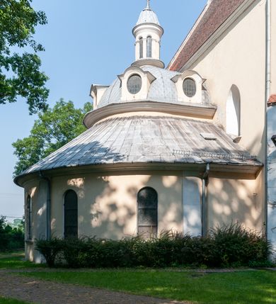 Zdjęcie nr 12: Budynek orientowany, jednonawowy. Prostokątna nawa jest szersza i znacznie wyższa, oddzielona od prezbiterium za pomocą ściany tarczowej z ostrołukową arkadą tęczową. Przy prezbiterium od północy zakrystia na planie prostokąta i taki sam skarbczyk, od południa niewielka, prostokątna kruchta. Przy nawie od południa podłużna kaplica Matki Boskiej Szkaplerznej (1741) z kwadratową kruchtą od zachodu; od północy kaplica Matki Boskiej Bolesnej na planie półokręgu z obejściem (1919-1932, projektu Bogdana Tretera). Prezbiterium sklepione krzyżowo-żebrowo, korpus sześciodzielnie, z gurtami. 
Okna nawy i kaplicy południowej ostrołukowe; w zwieńczeniu zakrystii jedno okno okrągłe; w kaplicy południowej okna zamknięte półkoliście, w kopule lukarny z eliptycznymi otworami okiennymi. 
Główne wejście od zachodu, ostrołukowe, drugie przez kruchtę od północy, w kształcie stojącego prostokąta. Portal z prezbiterium do zakrystii kamienny, profilowany zamknięty ściętym trójliściem (XV/XVI w.); portal z kruchty północnej do kaplicy kamienny, ostrołukowy, profilowany i fazowany, nad nim późnogotycka tarcza z herbem Nieczuja. Nad zewnętrznym, ostrołukowym portalem do kruchty północnej herb Korab i insygnia biskupa Jakuba Zadzika, pochodzące prawdopodobnie z dawnej bramy przejazdowej obok katedry w Kielcach. 
Na zewnątrz budynek opięty przyporami o zmiennym profilu. Elewacje, z wyjątkiem wschodniej ściany prezbiterium, tynkowane. Fasada zamknięta wysokim, trójkątnym szczytem, trójosiowa. W osi środkowej kamienny, ostrołukowy portal. W osiach bocznych ostrołukowe okna. Narożniki ujęte modelowanymi w tynku lizenami oraz przyporami. Powyżej na ich osiach prostopadłościenne sterczyny zwieńczone krzyżami. Elewacja wschodnia o analogicznym układzie, ceglana, nietynkowana, ujęta skośnie ustawionymi przyporami, jednoosiowa. W osi szeroka, jednouskokowa przypora z kamienną płyciną mieszczącą krucyfiks w dolnej części i analogiczną, mniejszą z kamienną figurą św. Piotra na tle okna powyżej. Na ścianie szczytowej cegły ułożone w jodełkę, w górnej części ostrołukowa, uskokowa płycina. Na zwieńczeniu wyryty napis „RENO/VATUM / A(NNO) D(OMINI)/ 1928”.  Elewacja północna z dobudowanymi na całej długości zakrystią, skarbczykiem i kaplicą. Elewacja południowa tynkowana, w części prezbiterium dwuosiowa; w narożniku pomiędzy prezbiterium a nawą niewielka kruchta. Do korpusu dobudowana kaplica – z tynkowanymi elewacjami o osiach podkreślonych lizenami, zróżnicowanymi kolorystycznie. Dach nad korpusem nawowym i prezbiterium dwuspadowy, nad zakrystią i skarbczykiem dachy pulpitowe –  kryte dachówką. Kaplica południowa nakryta kopułą z lunetami i latarnią – kryta blachą. Wieżyczka na sygnaturkę o formach barokowych z latarnią.