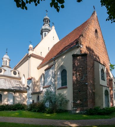 Zdjęcie nr 11: Budynek orientowany, jednonawowy. Prostokątna nawa jest szersza i znacznie wyższa, oddzielona od prezbiterium za pomocą ściany tarczowej z ostrołukową arkadą tęczową. Przy prezbiterium od północy zakrystia na planie prostokąta i taki sam skarbczyk, od południa niewielka, prostokątna kruchta. Przy nawie od południa podłużna kaplica Matki Boskiej Szkaplerznej (1741) z kwadratową kruchtą od zachodu; od północy kaplica Matki Boskiej Bolesnej na planie półokręgu z obejściem (1919-1932, projektu Bogdana Tretera). Prezbiterium sklepione krzyżowo-żebrowo, korpus sześciodzielnie, z gurtami. 
Okna nawy i kaplicy południowej ostrołukowe; w zwieńczeniu zakrystii jedno okno okrągłe; w kaplicy południowej okna zamknięte półkoliście, w kopule lukarny z eliptycznymi otworami okiennymi. 
Główne wejście od zachodu, ostrołukowe, drugie przez kruchtę od północy, w kształcie stojącego prostokąta. Portal z prezbiterium do zakrystii kamienny, profilowany zamknięty ściętym trójliściem (XV/XVI w.); portal z kruchty północnej do kaplicy kamienny, ostrołukowy, profilowany i fazowany, nad nim późnogotycka tarcza z herbem Nieczuja. Nad zewnętrznym, ostrołukowym portalem do kruchty północnej herb Korab i insygnia biskupa Jakuba Zadzika, pochodzące prawdopodobnie z dawnej bramy przejazdowej obok katedry w Kielcach. 
Na zewnątrz budynek opięty przyporami o zmiennym profilu. Elewacje, z wyjątkiem wschodniej ściany prezbiterium, tynkowane. Fasada zamknięta wysokim, trójkątnym szczytem, trójosiowa. W osi środkowej kamienny, ostrołukowy portal. W osiach bocznych ostrołukowe okna. Narożniki ujęte modelowanymi w tynku lizenami oraz przyporami. Powyżej na ich osiach prostopadłościenne sterczyny zwieńczone krzyżami. Elewacja wschodnia o analogicznym układzie, ceglana, nietynkowana, ujęta skośnie ustawionymi przyporami, jednoosiowa. W osi szeroka, jednouskokowa przypora z kamienną płyciną mieszczącą krucyfiks w dolnej części i analogiczną, mniejszą z kamienną figurą św. Piotra na tle okna powyżej. Na ścianie szczytowej cegły ułożone w jodełkę, w górnej części ostrołukowa, uskokowa płycina. Na zwieńczeniu wyryty napis „RENO/VATUM / A(NNO) D(OMINI)/ 1928”.  Elewacja północna z dobudowanymi na całej długości zakrystią, skarbczykiem i kaplicą. Elewacja południowa tynkowana, w części prezbiterium dwuosiowa; w narożniku pomiędzy prezbiterium a nawą niewielka kruchta. Do korpusu dobudowana kaplica – z tynkowanymi elewacjami o osiach podkreślonych lizenami, zróżnicowanymi kolorystycznie. Dach nad korpusem nawowym i prezbiterium dwuspadowy, nad zakrystią i skarbczykiem dachy pulpitowe –  kryte dachówką. Kaplica południowa nakryta kopułą z lunetami i latarnią – kryta blachą. Wieżyczka na sygnaturkę o formach barokowych z latarnią.