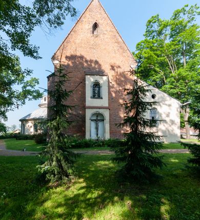 Zdjęcie nr 18: Budynek orientowany, jednonawowy. Prostokątna nawa jest szersza i znacznie wyższa, oddzielona od prezbiterium za pomocą ściany tarczowej z ostrołukową arkadą tęczową. Przy prezbiterium od północy zakrystia na planie prostokąta i taki sam skarbczyk, od południa niewielka, prostokątna kruchta. Przy nawie od południa podłużna kaplica Matki Boskiej Szkaplerznej (1741) z kwadratową kruchtą od zachodu; od północy kaplica Matki Boskiej Bolesnej na planie półokręgu z obejściem (1919-1932, projektu Bogdana Tretera). Prezbiterium sklepione krzyżowo-żebrowo, korpus sześciodzielnie, z gurtami. 
Okna nawy i kaplicy południowej ostrołukowe; w zwieńczeniu zakrystii jedno okno okrągłe; w kaplicy południowej okna zamknięte półkoliście, w kopule lukarny z eliptycznymi otworami okiennymi. 
Główne wejście od zachodu, ostrołukowe, drugie przez kruchtę od północy, w kształcie stojącego prostokąta. Portal z prezbiterium do zakrystii kamienny, profilowany zamknięty ściętym trójliściem (XV/XVI w.); portal z kruchty północnej do kaplicy kamienny, ostrołukowy, profilowany i fazowany, nad nim późnogotycka tarcza z herbem Nieczuja. Nad zewnętrznym, ostrołukowym portalem do kruchty północnej herb Korab i insygnia biskupa Jakuba Zadzika, pochodzące prawdopodobnie z dawnej bramy przejazdowej obok katedry w Kielcach. 
Na zewnątrz budynek opięty przyporami o zmiennym profilu. Elewacje, z wyjątkiem wschodniej ściany prezbiterium, tynkowane. Fasada zamknięta wysokim, trójkątnym szczytem, trójosiowa. W osi środkowej kamienny, ostrołukowy portal. W osiach bocznych ostrołukowe okna. Narożniki ujęte modelowanymi w tynku lizenami oraz przyporami. Powyżej na ich osiach prostopadłościenne sterczyny zwieńczone krzyżami. Elewacja wschodnia o analogicznym układzie, ceglana, nietynkowana, ujęta skośnie ustawionymi przyporami, jednoosiowa. W osi szeroka, jednouskokowa przypora z kamienną płyciną mieszczącą krucyfiks w dolnej części i analogiczną, mniejszą z kamienną figurą św. Piotra na tle okna powyżej. Na ścianie szczytowej cegły ułożone w jodełkę, w górnej części ostrołukowa, uskokowa płycina. Na zwieńczeniu wyryty napis „RENO/VATUM / A(NNO) D(OMINI)/ 1928”.  Elewacja północna z dobudowanymi na całej długości zakrystią, skarbczykiem i kaplicą. Elewacja południowa tynkowana, w części prezbiterium dwuosiowa; w narożniku pomiędzy prezbiterium a nawą niewielka kruchta. Do korpusu dobudowana kaplica – z tynkowanymi elewacjami o osiach podkreślonych lizenami, zróżnicowanymi kolorystycznie. Dach nad korpusem nawowym i prezbiterium dwuspadowy, nad zakrystią i skarbczykiem dachy pulpitowe –  kryte dachówką. Kaplica południowa nakryta kopułą z lunetami i latarnią – kryta blachą. Wieżyczka na sygnaturkę o formach barokowych z latarnią.