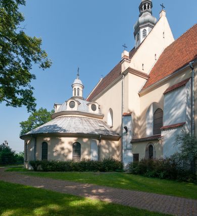 Zdjęcie nr 13: Budynek orientowany, jednonawowy. Prostokątna nawa jest szersza i znacznie wyższa, oddzielona od prezbiterium za pomocą ściany tarczowej z ostrołukową arkadą tęczową. Przy prezbiterium od północy zakrystia na planie prostokąta i taki sam skarbczyk, od południa niewielka, prostokątna kruchta. Przy nawie od południa podłużna kaplica Matki Boskiej Szkaplerznej (1741) z kwadratową kruchtą od zachodu; od północy kaplica Matki Boskiej Bolesnej na planie półokręgu z obejściem (1919-1932, projektu Bogdana Tretera). Prezbiterium sklepione krzyżowo-żebrowo, korpus sześciodzielnie, z gurtami. 
Okna nawy i kaplicy południowej ostrołukowe; w zwieńczeniu zakrystii jedno okno okrągłe; w kaplicy południowej okna zamknięte półkoliście, w kopule lukarny z eliptycznymi otworami okiennymi. 
Główne wejście od zachodu, ostrołukowe, drugie przez kruchtę od północy, w kształcie stojącego prostokąta. Portal z prezbiterium do zakrystii kamienny, profilowany zamknięty ściętym trójliściem (XV/XVI w.); portal z kruchty północnej do kaplicy kamienny, ostrołukowy, profilowany i fazowany, nad nim późnogotycka tarcza z herbem Nieczuja. Nad zewnętrznym, ostrołukowym portalem do kruchty północnej herb Korab i insygnia biskupa Jakuba Zadzika, pochodzące prawdopodobnie z dawnej bramy przejazdowej obok katedry w Kielcach. 
Na zewnątrz budynek opięty przyporami o zmiennym profilu. Elewacje, z wyjątkiem wschodniej ściany prezbiterium, tynkowane. Fasada zamknięta wysokim, trójkątnym szczytem, trójosiowa. W osi środkowej kamienny, ostrołukowy portal. W osiach bocznych ostrołukowe okna. Narożniki ujęte modelowanymi w tynku lizenami oraz przyporami. Powyżej na ich osiach prostopadłościenne sterczyny zwieńczone krzyżami. Elewacja wschodnia o analogicznym układzie, ceglana, nietynkowana, ujęta skośnie ustawionymi przyporami, jednoosiowa. W osi szeroka, jednouskokowa przypora z kamienną płyciną mieszczącą krucyfiks w dolnej części i analogiczną, mniejszą z kamienną figurą św. Piotra na tle okna powyżej. Na ścianie szczytowej cegły ułożone w jodełkę, w górnej części ostrołukowa, uskokowa płycina. Na zwieńczeniu wyryty napis „RENO/VATUM / A(NNO) D(OMINI)/ 1928”.  Elewacja północna z dobudowanymi na całej długości zakrystią, skarbczykiem i kaplicą. Elewacja południowa tynkowana, w części prezbiterium dwuosiowa; w narożniku pomiędzy prezbiterium a nawą niewielka kruchta. Do korpusu dobudowana kaplica – z tynkowanymi elewacjami o osiach podkreślonych lizenami, zróżnicowanymi kolorystycznie. Dach nad korpusem nawowym i prezbiterium dwuspadowy, nad zakrystią i skarbczykiem dachy pulpitowe –  kryte dachówką. Kaplica południowa nakryta kopułą z lunetami i latarnią – kryta blachą. Wieżyczka na sygnaturkę o formach barokowych z latarnią.