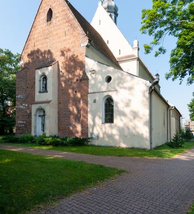 Zdjęcie nr 17: Budynek orientowany, jednonawowy. Prostokątna nawa jest szersza i znacznie wyższa, oddzielona od prezbiterium za pomocą ściany tarczowej z ostrołukową arkadą tęczową. Przy prezbiterium od północy zakrystia na planie prostokąta i taki sam skarbczyk, od południa niewielka, prostokątna kruchta. Przy nawie od południa podłużna kaplica Matki Boskiej Szkaplerznej (1741) z kwadratową kruchtą od zachodu; od północy kaplica Matki Boskiej Bolesnej na planie półokręgu z obejściem (1919-1932, projektu Bogdana Tretera). Prezbiterium sklepione krzyżowo-żebrowo, korpus sześciodzielnie, z gurtami. 
Okna nawy i kaplicy południowej ostrołukowe; w zwieńczeniu zakrystii jedno okno okrągłe; w kaplicy południowej okna zamknięte półkoliście, w kopule lukarny z eliptycznymi otworami okiennymi. 
Główne wejście od zachodu, ostrołukowe, drugie przez kruchtę od północy, w kształcie stojącego prostokąta. Portal z prezbiterium do zakrystii kamienny, profilowany zamknięty ściętym trójliściem (XV/XVI w.); portal z kruchty północnej do kaplicy kamienny, ostrołukowy, profilowany i fazowany, nad nim późnogotycka tarcza z herbem Nieczuja. Nad zewnętrznym, ostrołukowym portalem do kruchty północnej herb Korab i insygnia biskupa Jakuba Zadzika, pochodzące prawdopodobnie z dawnej bramy przejazdowej obok katedry w Kielcach. 
Na zewnątrz budynek opięty przyporami o zmiennym profilu. Elewacje, z wyjątkiem wschodniej ściany prezbiterium, tynkowane. Fasada zamknięta wysokim, trójkątnym szczytem, trójosiowa. W osi środkowej kamienny, ostrołukowy portal. W osiach bocznych ostrołukowe okna. Narożniki ujęte modelowanymi w tynku lizenami oraz przyporami. Powyżej na ich osiach prostopadłościenne sterczyny zwieńczone krzyżami. Elewacja wschodnia o analogicznym układzie, ceglana, nietynkowana, ujęta skośnie ustawionymi przyporami, jednoosiowa. W osi szeroka, jednouskokowa przypora z kamienną płyciną mieszczącą krucyfiks w dolnej części i analogiczną, mniejszą z kamienną figurą św. Piotra na tle okna powyżej. Na ścianie szczytowej cegły ułożone w jodełkę, w górnej części ostrołukowa, uskokowa płycina. Na zwieńczeniu wyryty napis „RENO/VATUM / A(NNO) D(OMINI)/ 1928”.  Elewacja północna z dobudowanymi na całej długości zakrystią, skarbczykiem i kaplicą. Elewacja południowa tynkowana, w części prezbiterium dwuosiowa; w narożniku pomiędzy prezbiterium a nawą niewielka kruchta. Do korpusu dobudowana kaplica – z tynkowanymi elewacjami o osiach podkreślonych lizenami, zróżnicowanymi kolorystycznie. Dach nad korpusem nawowym i prezbiterium dwuspadowy, nad zakrystią i skarbczykiem dachy pulpitowe –  kryte dachówką. Kaplica południowa nakryta kopułą z lunetami i latarnią – kryta blachą. Wieżyczka na sygnaturkę o formach barokowych z latarnią.