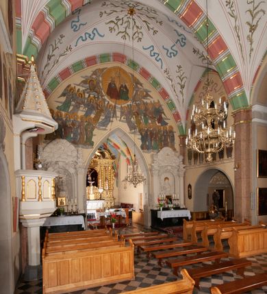 Zdjęcie nr 21: Budynek orientowany, jednonawowy. Prostokątna nawa jest szersza i znacznie wyższa, oddzielona od prezbiterium za pomocą ściany tarczowej z ostrołukową arkadą tęczową. Przy prezbiterium od północy zakrystia na planie prostokąta i taki sam skarbczyk, od południa niewielka, prostokątna kruchta. Przy nawie od południa podłużna kaplica Matki Boskiej Szkaplerznej (1741) z kwadratową kruchtą od zachodu; od północy kaplica Matki Boskiej Bolesnej na planie półokręgu z obejściem (1919-1932, projektu Bogdana Tretera). Prezbiterium sklepione krzyżowo-żebrowo, korpus sześciodzielnie, z gurtami. 
Okna nawy i kaplicy południowej ostrołukowe; w zwieńczeniu zakrystii jedno okno okrągłe; w kaplicy południowej okna zamknięte półkoliście, w kopule lukarny z eliptycznymi otworami okiennymi. 
Główne wejście od zachodu, ostrołukowe, drugie przez kruchtę od północy, w kształcie stojącego prostokąta. Portal z prezbiterium do zakrystii kamienny, profilowany zamknięty ściętym trójliściem (XV/XVI w.); portal z kruchty północnej do kaplicy kamienny, ostrołukowy, profilowany i fazowany, nad nim późnogotycka tarcza z herbem Nieczuja. Nad zewnętrznym, ostrołukowym portalem do kruchty północnej herb Korab i insygnia biskupa Jakuba Zadzika, pochodzące prawdopodobnie z dawnej bramy przejazdowej obok katedry w Kielcach. 
Na zewnątrz budynek opięty przyporami o zmiennym profilu. Elewacje, z wyjątkiem wschodniej ściany prezbiterium, tynkowane. Fasada zamknięta wysokim, trójkątnym szczytem, trójosiowa. W osi środkowej kamienny, ostrołukowy portal. W osiach bocznych ostrołukowe okna. Narożniki ujęte modelowanymi w tynku lizenami oraz przyporami. Powyżej na ich osiach prostopadłościenne sterczyny zwieńczone krzyżami. Elewacja wschodnia o analogicznym układzie, ceglana, nietynkowana, ujęta skośnie ustawionymi przyporami, jednoosiowa. W osi szeroka, jednouskokowa przypora z kamienną płyciną mieszczącą krucyfiks w dolnej części i analogiczną, mniejszą z kamienną figurą św. Piotra na tle okna powyżej. Na ścianie szczytowej cegły ułożone w jodełkę, w górnej części ostrołukowa, uskokowa płycina. Na zwieńczeniu wyryty napis „RENO/VATUM / A(NNO) D(OMINI)/ 1928”.  Elewacja północna z dobudowanymi na całej długości zakrystią, skarbczykiem i kaplicą. Elewacja południowa tynkowana, w części prezbiterium dwuosiowa; w narożniku pomiędzy prezbiterium a nawą niewielka kruchta. Do korpusu dobudowana kaplica – z tynkowanymi elewacjami o osiach podkreślonych lizenami, zróżnicowanymi kolorystycznie. Dach nad korpusem nawowym i prezbiterium dwuspadowy, nad zakrystią i skarbczykiem dachy pulpitowe –  kryte dachówką. Kaplica południowa nakryta kopułą z lunetami i latarnią – kryta blachą. Wieżyczka na sygnaturkę o formach barokowych z latarnią.