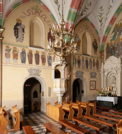 Zdjęcie nr 29: Budynek orientowany, jednonawowy. Prostokątna nawa jest szersza i znacznie wyższa, oddzielona od prezbiterium za pomocą ściany tarczowej z ostrołukową arkadą tęczową. Przy prezbiterium od północy zakrystia na planie prostokąta i taki sam skarbczyk, od południa niewielka, prostokątna kruchta. Przy nawie od południa podłużna kaplica Matki Boskiej Szkaplerznej (1741) z kwadratową kruchtą od zachodu; od północy kaplica Matki Boskiej Bolesnej na planie półokręgu z obejściem (1919-1932, projektu Bogdana Tretera). Prezbiterium sklepione krzyżowo-żebrowo, korpus sześciodzielnie, z gurtami. 
Okna nawy i kaplicy południowej ostrołukowe; w zwieńczeniu zakrystii jedno okno okrągłe; w kaplicy południowej okna zamknięte półkoliście, w kopule lukarny z eliptycznymi otworami okiennymi. 
Główne wejście od zachodu, ostrołukowe, drugie przez kruchtę od północy, w kształcie stojącego prostokąta. Portal z prezbiterium do zakrystii kamienny, profilowany zamknięty ściętym trójliściem (XV/XVI w.); portal z kruchty północnej do kaplicy kamienny, ostrołukowy, profilowany i fazowany, nad nim późnogotycka tarcza z herbem Nieczuja. Nad zewnętrznym, ostrołukowym portalem do kruchty północnej herb Korab i insygnia biskupa Jakuba Zadzika, pochodzące prawdopodobnie z dawnej bramy przejazdowej obok katedry w Kielcach. 
Na zewnątrz budynek opięty przyporami o zmiennym profilu. Elewacje, z wyjątkiem wschodniej ściany prezbiterium, tynkowane. Fasada zamknięta wysokim, trójkątnym szczytem, trójosiowa. W osi środkowej kamienny, ostrołukowy portal. W osiach bocznych ostrołukowe okna. Narożniki ujęte modelowanymi w tynku lizenami oraz przyporami. Powyżej na ich osiach prostopadłościenne sterczyny zwieńczone krzyżami. Elewacja wschodnia o analogicznym układzie, ceglana, nietynkowana, ujęta skośnie ustawionymi przyporami, jednoosiowa. W osi szeroka, jednouskokowa przypora z kamienną płyciną mieszczącą krucyfiks w dolnej części i analogiczną, mniejszą z kamienną figurą św. Piotra na tle okna powyżej. Na ścianie szczytowej cegły ułożone w jodełkę, w górnej części ostrołukowa, uskokowa płycina. Na zwieńczeniu wyryty napis „RENO/VATUM / A(NNO) D(OMINI)/ 1928”.  Elewacja północna z dobudowanymi na całej długości zakrystią, skarbczykiem i kaplicą. Elewacja południowa tynkowana, w części prezbiterium dwuosiowa; w narożniku pomiędzy prezbiterium a nawą niewielka kruchta. Do korpusu dobudowana kaplica – z tynkowanymi elewacjami o osiach podkreślonych lizenami, zróżnicowanymi kolorystycznie. Dach nad korpusem nawowym i prezbiterium dwuspadowy, nad zakrystią i skarbczykiem dachy pulpitowe –  kryte dachówką. Kaplica południowa nakryta kopułą z lunetami i latarnią – kryta blachą. Wieżyczka na sygnaturkę o formach barokowych z latarnią.