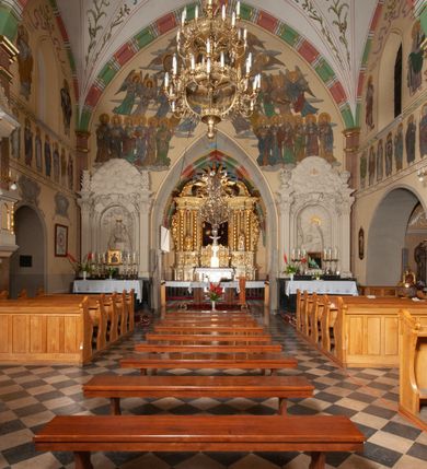 Zdjęcie nr 34: Budynek orientowany, jednonawowy. Prostokątna nawa jest szersza i znacznie wyższa, oddzielona od prezbiterium za pomocą ściany tarczowej z ostrołukową arkadą tęczową. Przy prezbiterium od północy zakrystia na planie prostokąta i taki sam skarbczyk, od południa niewielka, prostokątna kruchta. Przy nawie od południa podłużna kaplica Matki Boskiej Szkaplerznej (1741) z kwadratową kruchtą od zachodu; od północy kaplica Matki Boskiej Bolesnej na planie półokręgu z obejściem (1919-1932, projektu Bogdana Tretera). Prezbiterium sklepione krzyżowo-żebrowo, korpus sześciodzielnie, z gurtami. 
Okna nawy i kaplicy południowej ostrołukowe; w zwieńczeniu zakrystii jedno okno okrągłe; w kaplicy południowej okna zamknięte półkoliście, w kopule lukarny z eliptycznymi otworami okiennymi. 
Główne wejście od zachodu, ostrołukowe, drugie przez kruchtę od północy, w kształcie stojącego prostokąta. Portal z prezbiterium do zakrystii kamienny, profilowany zamknięty ściętym trójliściem (XV/XVI w.); portal z kruchty północnej do kaplicy kamienny, ostrołukowy, profilowany i fazowany, nad nim późnogotycka tarcza z herbem Nieczuja. Nad zewnętrznym, ostrołukowym portalem do kruchty północnej herb Korab i insygnia biskupa Jakuba Zadzika, pochodzące prawdopodobnie z dawnej bramy przejazdowej obok katedry w Kielcach. 
Na zewnątrz budynek opięty przyporami o zmiennym profilu. Elewacje, z wyjątkiem wschodniej ściany prezbiterium, tynkowane. Fasada zamknięta wysokim, trójkątnym szczytem, trójosiowa. W osi środkowej kamienny, ostrołukowy portal. W osiach bocznych ostrołukowe okna. Narożniki ujęte modelowanymi w tynku lizenami oraz przyporami. Powyżej na ich osiach prostopadłościenne sterczyny zwieńczone krzyżami. Elewacja wschodnia o analogicznym układzie, ceglana, nietynkowana, ujęta skośnie ustawionymi przyporami, jednoosiowa. W osi szeroka, jednouskokowa przypora z kamienną płyciną mieszczącą krucyfiks w dolnej części i analogiczną, mniejszą z kamienną figurą św. Piotra na tle okna powyżej. Na ścianie szczytowej cegły ułożone w jodełkę, w górnej części ostrołukowa, uskokowa płycina. Na zwieńczeniu wyryty napis „RENO/VATUM / A(NNO) D(OMINI)/ 1928”.  Elewacja północna z dobudowanymi na całej długości zakrystią, skarbczykiem i kaplicą. Elewacja południowa tynkowana, w części prezbiterium dwuosiowa; w narożniku pomiędzy prezbiterium a nawą niewielka kruchta. Do korpusu dobudowana kaplica – z tynkowanymi elewacjami o osiach podkreślonych lizenami, zróżnicowanymi kolorystycznie. Dach nad korpusem nawowym i prezbiterium dwuspadowy, nad zakrystią i skarbczykiem dachy pulpitowe –  kryte dachówką. Kaplica południowa nakryta kopułą z lunetami i latarnią – kryta blachą. Wieżyczka na sygnaturkę o formach barokowych z latarnią.