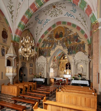 Zdjęcie nr 33: Budynek orientowany, jednonawowy. Prostokątna nawa jest szersza i znacznie wyższa, oddzielona od prezbiterium za pomocą ściany tarczowej z ostrołukową arkadą tęczową. Przy prezbiterium od północy zakrystia na planie prostokąta i taki sam skarbczyk, od południa niewielka, prostokątna kruchta. Przy nawie od południa podłużna kaplica Matki Boskiej Szkaplerznej (1741) z kwadratową kruchtą od zachodu; od północy kaplica Matki Boskiej Bolesnej na planie półokręgu z obejściem (1919-1932, projektu Bogdana Tretera). Prezbiterium sklepione krzyżowo-żebrowo, korpus sześciodzielnie, z gurtami. 
Okna nawy i kaplicy południowej ostrołukowe; w zwieńczeniu zakrystii jedno okno okrągłe; w kaplicy południowej okna zamknięte półkoliście, w kopule lukarny z eliptycznymi otworami okiennymi. 
Główne wejście od zachodu, ostrołukowe, drugie przez kruchtę od północy, w kształcie stojącego prostokąta. Portal z prezbiterium do zakrystii kamienny, profilowany zamknięty ściętym trójliściem (XV/XVI w.); portal z kruchty północnej do kaplicy kamienny, ostrołukowy, profilowany i fazowany, nad nim późnogotycka tarcza z herbem Nieczuja. Nad zewnętrznym, ostrołukowym portalem do kruchty północnej herb Korab i insygnia biskupa Jakuba Zadzika, pochodzące prawdopodobnie z dawnej bramy przejazdowej obok katedry w Kielcach. 
Na zewnątrz budynek opięty przyporami o zmiennym profilu. Elewacje, z wyjątkiem wschodniej ściany prezbiterium, tynkowane. Fasada zamknięta wysokim, trójkątnym szczytem, trójosiowa. W osi środkowej kamienny, ostrołukowy portal. W osiach bocznych ostrołukowe okna. Narożniki ujęte modelowanymi w tynku lizenami oraz przyporami. Powyżej na ich osiach prostopadłościenne sterczyny zwieńczone krzyżami. Elewacja wschodnia o analogicznym układzie, ceglana, nietynkowana, ujęta skośnie ustawionymi przyporami, jednoosiowa. W osi szeroka, jednouskokowa przypora z kamienną płyciną mieszczącą krucyfiks w dolnej części i analogiczną, mniejszą z kamienną figurą św. Piotra na tle okna powyżej. Na ścianie szczytowej cegły ułożone w jodełkę, w górnej części ostrołukowa, uskokowa płycina. Na zwieńczeniu wyryty napis „RENO/VATUM / A(NNO) D(OMINI)/ 1928”.  Elewacja północna z dobudowanymi na całej długości zakrystią, skarbczykiem i kaplicą. Elewacja południowa tynkowana, w części prezbiterium dwuosiowa; w narożniku pomiędzy prezbiterium a nawą niewielka kruchta. Do korpusu dobudowana kaplica – z tynkowanymi elewacjami o osiach podkreślonych lizenami, zróżnicowanymi kolorystycznie. Dach nad korpusem nawowym i prezbiterium dwuspadowy, nad zakrystią i skarbczykiem dachy pulpitowe –  kryte dachówką. Kaplica południowa nakryta kopułą z lunetami i latarnią – kryta blachą. Wieżyczka na sygnaturkę o formach barokowych z latarnią.