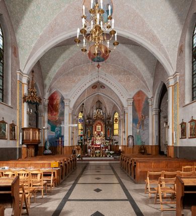 Zdjęcie nr 16: Kościół murowany z cegły, tynkowany, orientowany z odchyleniem ku północy. Zbudowany na planie krzyża łacińskiego, jednonawowy z transeptem, pięcioprzęsłowy, z jednoprzęsłowym prezbiterium zamkniętym trójbocznie. Sklepienie beczkowe spłaszczone (koszowe) na gurtach z lunetami stykającymi się wierzchołkami. W pierwszym od zachodu przęśle nawy chór muzyczny konstrukcji żelbetowej wsparty na dwóch filarach o przekroju ośmioboku i dwóch analogicznych półfilarach. Balustrada artykułowana ostrołukowymi niszami. Ściany boczne rozczłonkowane analogicznymi półfilarami, ustawionymi na tle pilastrów; proste kapitele toskańskie. Ściana tęczowa z arkadą ostrołukową, ujętą po bokach dwoma mniejszymi ostrołukowymi płycinami. Od zachodu prostokątna kruchta z dwoma ostrołukowymi otworami drzwiowymi. Mniejsza prostokątna kruchta od południa, skomunikowana z nawą kamiennym, profilowanym portalem prostokątnym. W prezbiterium od południa prostokątny otwór wejściowy do zakrystii. Okna obustronnie rozglifione, z  parapetami, o kształcie wydłużonego prostokąta, zamkniętego ostrołukowo; po trzy w ścianach bocznych nawy, trzy w prezbiterium. Dwa mniejsze w fasadzie kościoła, po jednym na ścianach bocznych kruchty zachodniej. W zamknięciu ścian transeptu, większe ostrołukowe okna z podziałami kamiennymi dzielącymi okno na dwie, mniejsze, przedzielone półfilarem, zamknięte ostrołukowo części. Kościół nakryty dachem dwuspadowym z blachy. Fasada bezwieżowa z trójkątnym szczytem. Na zewnętrznej, wschodniej ścianie prezbiterium niewielka kwadratowa płycina z inskrypcją: „KAMIEŃ / WĘGIELNY / POŚWIĘCONY / DN(IA) 21 VI 1936”.