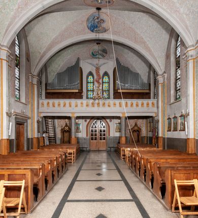 Zdjęcie nr 32: Kościół murowany z cegły, tynkowany, orientowany z odchyleniem ku północy. Zbudowany na planie krzyża łacińskiego, jednonawowy z transeptem, pięcioprzęsłowy, z jednoprzęsłowym prezbiterium zamkniętym trójbocznie. Sklepienie beczkowe spłaszczone (koszowe) na gurtach z lunetami stykającymi się wierzchołkami. W pierwszym od zachodu przęśle nawy chór muzyczny konstrukcji żelbetowej wsparty na dwóch filarach o przekroju ośmioboku i dwóch analogicznych półfilarach. Balustrada artykułowana ostrołukowymi niszami. Ściany boczne rozczłonkowane analogicznymi półfilarami, ustawionymi na tle pilastrów; proste kapitele toskańskie. Ściana tęczowa z arkadą ostrołukową, ujętą po bokach dwoma mniejszymi ostrołukowymi płycinami. Od zachodu prostokątna kruchta z dwoma ostrołukowymi otworami drzwiowymi. Mniejsza prostokątna kruchta od południa, skomunikowana z nawą kamiennym, profilowanym portalem prostokątnym. W prezbiterium od południa prostokątny otwór wejściowy do zakrystii. Okna obustronnie rozglifione, z  parapetami, o kształcie wydłużonego prostokąta, zamkniętego ostrołukowo; po trzy w ścianach bocznych nawy, trzy w prezbiterium. Dwa mniejsze w fasadzie kościoła, po jednym na ścianach bocznych kruchty zachodniej. W zamknięciu ścian transeptu, większe ostrołukowe okna z podziałami kamiennymi dzielącymi okno na dwie, mniejsze, przedzielone półfilarem, zamknięte ostrołukowo części. Kościół nakryty dachem dwuspadowym z blachy. Fasada bezwieżowa z trójkątnym szczytem. Na zewnętrznej, wschodniej ścianie prezbiterium niewielka kwadratowa płycina z inskrypcją: „KAMIEŃ / WĘGIELNY / POŚWIĘCONY / DN(IA) 21 VI 1936”.