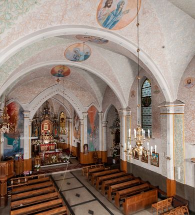 Zdjęcie nr 20: Kościół murowany z cegły, tynkowany, orientowany z odchyleniem ku północy. Zbudowany na planie krzyża łacińskiego, jednonawowy z transeptem, pięcioprzęsłowy, z jednoprzęsłowym prezbiterium zamkniętym trójbocznie. Sklepienie beczkowe spłaszczone (koszowe) na gurtach z lunetami stykającymi się wierzchołkami. W pierwszym od zachodu przęśle nawy chór muzyczny konstrukcji żelbetowej wsparty na dwóch filarach o przekroju ośmioboku i dwóch analogicznych półfilarach. Balustrada artykułowana ostrołukowymi niszami. Ściany boczne rozczłonkowane analogicznymi półfilarami, ustawionymi na tle pilastrów; proste kapitele toskańskie. Ściana tęczowa z arkadą ostrołukową, ujętą po bokach dwoma mniejszymi ostrołukowymi płycinami. Od zachodu prostokątna kruchta z dwoma ostrołukowymi otworami drzwiowymi. Mniejsza prostokątna kruchta od południa, skomunikowana z nawą kamiennym, profilowanym portalem prostokątnym. W prezbiterium od południa prostokątny otwór wejściowy do zakrystii. Okna obustronnie rozglifione, z  parapetami, o kształcie wydłużonego prostokąta, zamkniętego ostrołukowo; po trzy w ścianach bocznych nawy, trzy w prezbiterium. Dwa mniejsze w fasadzie kościoła, po jednym na ścianach bocznych kruchty zachodniej. W zamknięciu ścian transeptu, większe ostrołukowe okna z podziałami kamiennymi dzielącymi okno na dwie, mniejsze, przedzielone półfilarem, zamknięte ostrołukowo części. Kościół nakryty dachem dwuspadowym z blachy. Fasada bezwieżowa z trójkątnym szczytem. Na zewnętrznej, wschodniej ścianie prezbiterium niewielka kwadratowa płycina z inskrypcją: „KAMIEŃ / WĘGIELNY / POŚWIĘCONY / DN(IA) 21 VI 1936”.