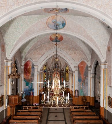 Zdjęcie nr 28: Kościół murowany z cegły, tynkowany, orientowany z odchyleniem ku północy. Zbudowany na planie krzyża łacińskiego, jednonawowy z transeptem, pięcioprzęsłowy, z jednoprzęsłowym prezbiterium zamkniętym trójbocznie. Sklepienie beczkowe spłaszczone (koszowe) na gurtach z lunetami stykającymi się wierzchołkami. W pierwszym od zachodu przęśle nawy chór muzyczny konstrukcji żelbetowej wsparty na dwóch filarach o przekroju ośmioboku i dwóch analogicznych półfilarach. Balustrada artykułowana ostrołukowymi niszami. Ściany boczne rozczłonkowane analogicznymi półfilarami, ustawionymi na tle pilastrów; proste kapitele toskańskie. Ściana tęczowa z arkadą ostrołukową, ujętą po bokach dwoma mniejszymi ostrołukowymi płycinami. Od zachodu prostokątna kruchta z dwoma ostrołukowymi otworami drzwiowymi. Mniejsza prostokątna kruchta od południa, skomunikowana z nawą kamiennym, profilowanym portalem prostokątnym. W prezbiterium od południa prostokątny otwór wejściowy do zakrystii. Okna obustronnie rozglifione, z  parapetami, o kształcie wydłużonego prostokąta, zamkniętego ostrołukowo; po trzy w ścianach bocznych nawy, trzy w prezbiterium. Dwa mniejsze w fasadzie kościoła, po jednym na ścianach bocznych kruchty zachodniej. W zamknięciu ścian transeptu, większe ostrołukowe okna z podziałami kamiennymi dzielącymi okno na dwie, mniejsze, przedzielone półfilarem, zamknięte ostrołukowo części. Kościół nakryty dachem dwuspadowym z blachy. Fasada bezwieżowa z trójkątnym szczytem. Na zewnętrznej, wschodniej ścianie prezbiterium niewielka kwadratowa płycina z inskrypcją: „KAMIEŃ / WĘGIELNY / POŚWIĘCONY / DN(IA) 21 VI 1936”.