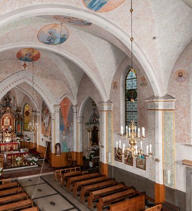 Zdjęcie nr 23: Kościół murowany z cegły, tynkowany, orientowany z odchyleniem ku północy. Zbudowany na planie krzyża łacińskiego, jednonawowy z transeptem, pięcioprzęsłowy, z jednoprzęsłowym prezbiterium zamkniętym trójbocznie. Sklepienie beczkowe spłaszczone (koszowe) na gurtach z lunetami stykającymi się wierzchołkami. W pierwszym od zachodu przęśle nawy chór muzyczny konstrukcji żelbetowej wsparty na dwóch filarach o przekroju ośmioboku i dwóch analogicznych półfilarach. Balustrada artykułowana ostrołukowymi niszami. Ściany boczne rozczłonkowane analogicznymi półfilarami, ustawionymi na tle pilastrów; proste kapitele toskańskie. Ściana tęczowa z arkadą ostrołukową, ujętą po bokach dwoma mniejszymi ostrołukowymi płycinami. Od zachodu prostokątna kruchta z dwoma ostrołukowymi otworami drzwiowymi. Mniejsza prostokątna kruchta od południa, skomunikowana z nawą kamiennym, profilowanym portalem prostokątnym. W prezbiterium od południa prostokątny otwór wejściowy do zakrystii. Okna obustronnie rozglifione, z  parapetami, o kształcie wydłużonego prostokąta, zamkniętego ostrołukowo; po trzy w ścianach bocznych nawy, trzy w prezbiterium. Dwa mniejsze w fasadzie kościoła, po jednym na ścianach bocznych kruchty zachodniej. W zamknięciu ścian transeptu, większe ostrołukowe okna z podziałami kamiennymi dzielącymi okno na dwie, mniejsze, przedzielone półfilarem, zamknięte ostrołukowo części. Kościół nakryty dachem dwuspadowym z blachy. Fasada bezwieżowa z trójkątnym szczytem. Na zewnętrznej, wschodniej ścianie prezbiterium niewielka kwadratowa płycina z inskrypcją: „KAMIEŃ / WĘGIELNY / POŚWIĘCONY / DN(IA) 21 VI 1936”.