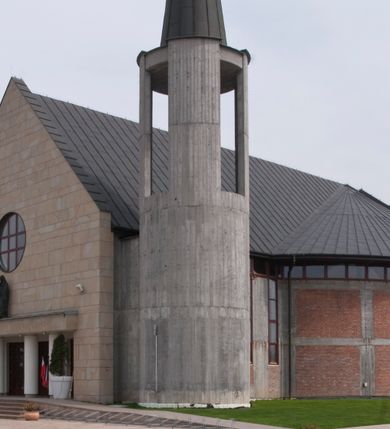 Zdjęcie nr 2: Kościół usytuowany na dużej działce o nieregularnym kształcie.  Świątynia otoczona trawnikiem, w którym wydzielono niewielkie klomby kwiatowe i ciągi komunikacyjne. Kościół orientowany, jednonawowy, jednoprzestrzenny z prezbiterium zamkniętym od zewnątrz szeroką absydą. Ściany boczne nawy od strony wschodniej założone na planie odcinka koła. Wnętrze jednoprzestrzenne, z widoczną konstrukcją otwartej więźby dachowej. Widoczne, drewniane belki wspierające się na 12 kolumnach, ustawionych w dwa rzędy, w układzie powtarzających rytm ścian. Prezbiterium na trójstopniowym wzniesieniu, oddzielone od nawy ścianą tęczową, zamknięte prostą ścianą. Od strony zachodniej chór muzyczny konstrukcji żelbetowej o pełnym, prostym parapecie, wsparty na dwóch okrągłych filarach. Po cztery pionowe okna łączące się w górnych partiach z świetlikiem obiegającym całą nawę. Mury zakończone uproszczonym gzymsem. W północno-zachodnim narożu niewielka kaplica Jana Pawła II, założona na planie koła. Fasada kościoła z trójkątną ścianą szczytową wyłożoną okładziną kamienną z umieszczonym w osi dużym okrągłym oknem, ujęta dwoma betonowymi wieżami na planie koła. W górnej części wieże z prześwitami na dzwony, nakryte strzelistymi, ostrosłupowymi dachami. W przyziemiu portyk wejściowy w formie czterech kolumn dźwigających masywny gzyms z napisem: „KOŚCIÓŁ MATKI BOSKIEJ RÓŻAŃCOWEJ”, powyżej rzeźba Madonny z Dzieciątkiem. 

