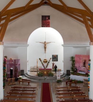 Zdjęcie nr 13: Kościół usytuowany na dużej działce o nieregularnym kształcie.  Świątynia otoczona trawnikiem, w którym wydzielono niewielkie klomby kwiatowe i ciągi komunikacyjne. Kościół orientowany, jednonawowy, jednoprzestrzenny z prezbiterium zamkniętym od zewnątrz szeroką absydą. Ściany boczne nawy od strony wschodniej założone na planie odcinka koła. Wnętrze jednoprzestrzenne, z widoczną konstrukcją otwartej więźby dachowej. Widoczne, drewniane belki wspierające się na 12 kolumnach, ustawionych w dwa rzędy, w układzie powtarzających rytm ścian. Prezbiterium na trójstopniowym wzniesieniu, oddzielone od nawy ścianą tęczową, zamknięte prostą ścianą. Od strony zachodniej chór muzyczny konstrukcji żelbetowej o pełnym, prostym parapecie, wsparty na dwóch okrągłych filarach. Po cztery pionowe okna łączące się w górnych partiach z świetlikiem obiegającym całą nawę. Mury zakończone uproszczonym gzymsem. W północno-zachodnim narożu niewielka kaplica Jana Pawła II, założona na planie koła. Fasada kościoła z trójkątną ścianą szczytową wyłożoną okładziną kamienną z umieszczonym w osi dużym okrągłym oknem, ujęta dwoma betonowymi wieżami na planie koła. W górnej części wieże z prześwitami na dzwony, nakryte strzelistymi, ostrosłupowymi dachami. W przyziemiu portyk wejściowy w formie czterech kolumn dźwigających masywny gzyms z napisem: „KOŚCIÓŁ MATKI BOSKIEJ RÓŻAŃCOWEJ”, powyżej rzeźba Madonny z Dzieciątkiem. 

