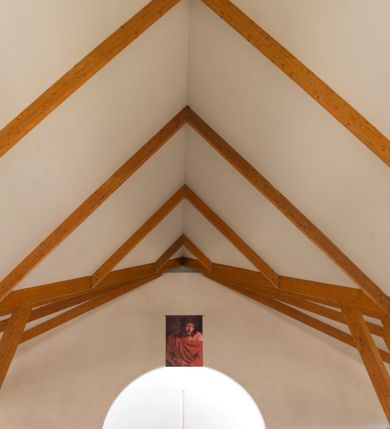 Zdjęcie nr 27: Kościół usytuowany na dużej działce o nieregularnym kształcie.  Świątynia otoczona trawnikiem, w którym wydzielono niewielkie klomby kwiatowe i ciągi komunikacyjne. Kościół orientowany, jednonawowy, jednoprzestrzenny z prezbiterium zamkniętym od zewnątrz szeroką absydą. Ściany boczne nawy od strony wschodniej założone na planie odcinka koła. Wnętrze jednoprzestrzenne, z widoczną konstrukcją otwartej więźby dachowej. Widoczne, drewniane belki wspierające się na 12 kolumnach, ustawionych w dwa rzędy, w układzie powtarzających rytm ścian. Prezbiterium na trójstopniowym wzniesieniu, oddzielone od nawy ścianą tęczową, zamknięte prostą ścianą. Od strony zachodniej chór muzyczny konstrukcji żelbetowej o pełnym, prostym parapecie, wsparty na dwóch okrągłych filarach. Po cztery pionowe okna łączące się w górnych partiach z świetlikiem obiegającym całą nawę. Mury zakończone uproszczonym gzymsem. W północno-zachodnim narożu niewielka kaplica Jana Pawła II, założona na planie koła. Fasada kościoła z trójkątną ścianą szczytową wyłożoną okładziną kamienną z umieszczonym w osi dużym okrągłym oknem, ujęta dwoma betonowymi wieżami na planie koła. W górnej części wieże z prześwitami na dzwony, nakryte strzelistymi, ostrosłupowymi dachami. W przyziemiu portyk wejściowy w formie czterech kolumn dźwigających masywny gzyms z napisem: „KOŚCIÓŁ MATKI BOSKIEJ RÓŻAŃCOWEJ”, powyżej rzeźba Madonny z Dzieciątkiem. 

