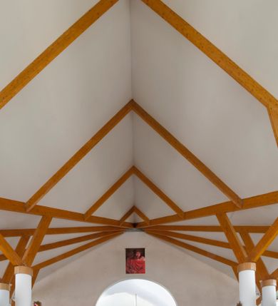 Zdjęcie nr 26: Kościół usytuowany na dużej działce o nieregularnym kształcie.  Świątynia otoczona trawnikiem, w którym wydzielono niewielkie klomby kwiatowe i ciągi komunikacyjne. Kościół orientowany, jednonawowy, jednoprzestrzenny z prezbiterium zamkniętym od zewnątrz szeroką absydą. Ściany boczne nawy od strony wschodniej założone na planie odcinka koła. Wnętrze jednoprzestrzenne, z widoczną konstrukcją otwartej więźby dachowej. Widoczne, drewniane belki wspierające się na 12 kolumnach, ustawionych w dwa rzędy, w układzie powtarzających rytm ścian. Prezbiterium na trójstopniowym wzniesieniu, oddzielone od nawy ścianą tęczową, zamknięte prostą ścianą. Od strony zachodniej chór muzyczny konstrukcji żelbetowej o pełnym, prostym parapecie, wsparty na dwóch okrągłych filarach. Po cztery pionowe okna łączące się w górnych partiach z świetlikiem obiegającym całą nawę. Mury zakończone uproszczonym gzymsem. W północno-zachodnim narożu niewielka kaplica Jana Pawła II, założona na planie koła. Fasada kościoła z trójkątną ścianą szczytową wyłożoną okładziną kamienną z umieszczonym w osi dużym okrągłym oknem, ujęta dwoma betonowymi wieżami na planie koła. W górnej części wieże z prześwitami na dzwony, nakryte strzelistymi, ostrosłupowymi dachami. W przyziemiu portyk wejściowy w formie czterech kolumn dźwigających masywny gzyms z napisem: „KOŚCIÓŁ MATKI BOSKIEJ RÓŻAŃCOWEJ”, powyżej rzeźba Madonny z Dzieciątkiem. 

