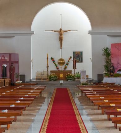 Zdjęcie nr 20: Kościół usytuowany na dużej działce o nieregularnym kształcie.  Świątynia otoczona trawnikiem, w którym wydzielono niewielkie klomby kwiatowe i ciągi komunikacyjne. Kościół orientowany, jednonawowy, jednoprzestrzenny z prezbiterium zamkniętym od zewnątrz szeroką absydą. Ściany boczne nawy od strony wschodniej założone na planie odcinka koła. Wnętrze jednoprzestrzenne, z widoczną konstrukcją otwartej więźby dachowej. Widoczne, drewniane belki wspierające się na 12 kolumnach, ustawionych w dwa rzędy, w układzie powtarzających rytm ścian. Prezbiterium na trójstopniowym wzniesieniu, oddzielone od nawy ścianą tęczową, zamknięte prostą ścianą. Od strony zachodniej chór muzyczny konstrukcji żelbetowej o pełnym, prostym parapecie, wsparty na dwóch okrągłych filarach. Po cztery pionowe okna łączące się w górnych partiach z świetlikiem obiegającym całą nawę. Mury zakończone uproszczonym gzymsem. W północno-zachodnim narożu niewielka kaplica Jana Pawła II, założona na planie koła. Fasada kościoła z trójkątną ścianą szczytową wyłożoną okładziną kamienną z umieszczonym w osi dużym okrągłym oknem, ujęta dwoma betonowymi wieżami na planie koła. W górnej części wieże z prześwitami na dzwony, nakryte strzelistymi, ostrosłupowymi dachami. W przyziemiu portyk wejściowy w formie czterech kolumn dźwigających masywny gzyms z napisem: „KOŚCIÓŁ MATKI BOSKIEJ RÓŻAŃCOWEJ”, powyżej rzeźba Madonny z Dzieciątkiem. 

