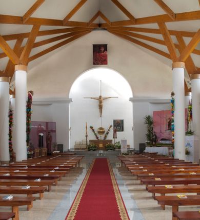 Zdjęcie nr 23: Kościół usytuowany na dużej działce o nieregularnym kształcie.  Świątynia otoczona trawnikiem, w którym wydzielono niewielkie klomby kwiatowe i ciągi komunikacyjne. Kościół orientowany, jednonawowy, jednoprzestrzenny z prezbiterium zamkniętym od zewnątrz szeroką absydą. Ściany boczne nawy od strony wschodniej założone na planie odcinka koła. Wnętrze jednoprzestrzenne, z widoczną konstrukcją otwartej więźby dachowej. Widoczne, drewniane belki wspierające się na 12 kolumnach, ustawionych w dwa rzędy, w układzie powtarzających rytm ścian. Prezbiterium na trójstopniowym wzniesieniu, oddzielone od nawy ścianą tęczową, zamknięte prostą ścianą. Od strony zachodniej chór muzyczny konstrukcji żelbetowej o pełnym, prostym parapecie, wsparty na dwóch okrągłych filarach. Po cztery pionowe okna łączące się w górnych partiach z świetlikiem obiegającym całą nawę. Mury zakończone uproszczonym gzymsem. W północno-zachodnim narożu niewielka kaplica Jana Pawła II, założona na planie koła. Fasada kościoła z trójkątną ścianą szczytową wyłożoną okładziną kamienną z umieszczonym w osi dużym okrągłym oknem, ujęta dwoma betonowymi wieżami na planie koła. W górnej części wieże z prześwitami na dzwony, nakryte strzelistymi, ostrosłupowymi dachami. W przyziemiu portyk wejściowy w formie czterech kolumn dźwigających masywny gzyms z napisem: „KOŚCIÓŁ MATKI BOSKIEJ RÓŻAŃCOWEJ”, powyżej rzeźba Madonny z Dzieciątkiem. 

