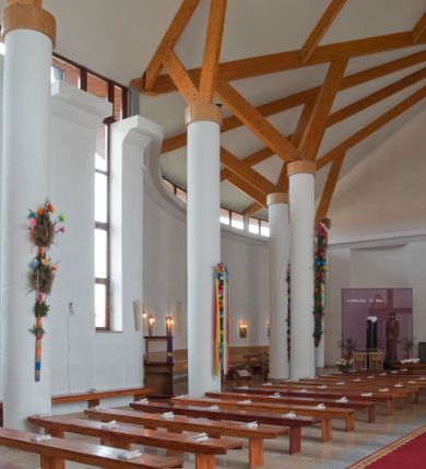 Zdjęcie nr 21: Kościół usytuowany na dużej działce o nieregularnym kształcie.  Świątynia otoczona trawnikiem, w którym wydzielono niewielkie klomby kwiatowe i ciągi komunikacyjne. Kościół orientowany, jednonawowy, jednoprzestrzenny z prezbiterium zamkniętym od zewnątrz szeroką absydą. Ściany boczne nawy od strony wschodniej założone na planie odcinka koła. Wnętrze jednoprzestrzenne, z widoczną konstrukcją otwartej więźby dachowej. Widoczne, drewniane belki wspierające się na 12 kolumnach, ustawionych w dwa rzędy, w układzie powtarzających rytm ścian. Prezbiterium na trójstopniowym wzniesieniu, oddzielone od nawy ścianą tęczową, zamknięte prostą ścianą. Od strony zachodniej chór muzyczny konstrukcji żelbetowej o pełnym, prostym parapecie, wsparty na dwóch okrągłych filarach. Po cztery pionowe okna łączące się w górnych partiach z świetlikiem obiegającym całą nawę. Mury zakończone uproszczonym gzymsem. W północno-zachodnim narożu niewielka kaplica Jana Pawła II, założona na planie koła. Fasada kościoła z trójkątną ścianą szczytową wyłożoną okładziną kamienną z umieszczonym w osi dużym okrągłym oknem, ujęta dwoma betonowymi wieżami na planie koła. W górnej części wieże z prześwitami na dzwony, nakryte strzelistymi, ostrosłupowymi dachami. W przyziemiu portyk wejściowy w formie czterech kolumn dźwigających masywny gzyms z napisem: „KOŚCIÓŁ MATKI BOSKIEJ RÓŻAŃCOWEJ”, powyżej rzeźba Madonny z Dzieciątkiem. 

