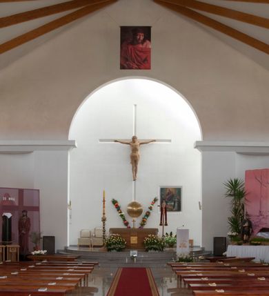 Zdjęcie nr 19: Kościół usytuowany na dużej działce o nieregularnym kształcie.  Świątynia otoczona trawnikiem, w którym wydzielono niewielkie klomby kwiatowe i ciągi komunikacyjne. Kościół orientowany, jednonawowy, jednoprzestrzenny z prezbiterium zamkniętym od zewnątrz szeroką absydą. Ściany boczne nawy od strony wschodniej założone na planie odcinka koła. Wnętrze jednoprzestrzenne, z widoczną konstrukcją otwartej więźby dachowej. Widoczne, drewniane belki wspierające się na 12 kolumnach, ustawionych w dwa rzędy, w układzie powtarzających rytm ścian. Prezbiterium na trójstopniowym wzniesieniu, oddzielone od nawy ścianą tęczową, zamknięte prostą ścianą. Od strony zachodniej chór muzyczny konstrukcji żelbetowej o pełnym, prostym parapecie, wsparty na dwóch okrągłych filarach. Po cztery pionowe okna łączące się w górnych partiach z świetlikiem obiegającym całą nawę. Mury zakończone uproszczonym gzymsem. W północno-zachodnim narożu niewielka kaplica Jana Pawła II, założona na planie koła. Fasada kościoła z trójkątną ścianą szczytową wyłożoną okładziną kamienną z umieszczonym w osi dużym okrągłym oknem, ujęta dwoma betonowymi wieżami na planie koła. W górnej części wieże z prześwitami na dzwony, nakryte strzelistymi, ostrosłupowymi dachami. W przyziemiu portyk wejściowy w formie czterech kolumn dźwigających masywny gzyms z napisem: „KOŚCIÓŁ MATKI BOSKIEJ RÓŻAŃCOWEJ”, powyżej rzeźba Madonny z Dzieciątkiem. 

