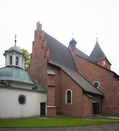 Zdjęcie nr 23: Na miejscu kościoła romańskiego, orientowany, dwunawowy, halowy; nawa południowa na rzucie prostokąta, na osi prezbiterium, dwuprzęsłowa, sklepiona kolebkowo z lunetami, na gurtach; nawa północna węższa od południowej, dwuprzęsłowa, sklepiona krzyżowo-żebrowo z kolistymi płaskorzeźbionymi zwornikami, jeden z literami ihs, drugi z literą s pod koroną. Prezbiterium prostokątne, dwuprzęsłowe, sklepione krzyżowo-żebrowo, z kolistymi zwornikami i profilowanymi wspornikami; przy nim od północy dawna zakrystia na rzucie prostokąta, sklepiona kolebkowo, otwarta do nawy wtórną arkadą, od wschodu nowa zakrystia na rzucie ośmioboku. Od zachodu przylega do nawy kwadratowa, czterokondygnacyjna wieża, z wieżyczką schodową w narożu północno-wschodnim, kruchtą w przyziemiu i chórem muzycznym na piętrze. Przy niej od północy drewniana piętrowa przybudówka mieszcząca w przyziemiu komorę bracką, na piętrze miech i kanał organowy. Przy nawie południowej od południa kwadratowa kruchta. Arkada tęczy zamknięta łukiem półkolistym, arkady do nawy północnej łukiem lekko zaostrzonym. Mury opięte przyporami, elewacje na cokole, z wzorami z zendrówki. Okna pierwotnie ostrołukowe, obustronnie rozglifione (niektóre zbarokizowane). Portale: zachodni, do kruchty pod wieżą, oraz do kruchty południowej, kamienne, prostokątne. Dachy dwuspadowe, pokryte blachą miedzianą. Zakrystia od wschodu przy prezbiterium wzniesiona na miejscu drewnianej kaplicy Ogrojcowej z XVIII wieku.