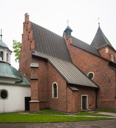 Zdjęcie nr 20: Na miejscu kościoła romańskiego, orientowany, dwunawowy, halowy; nawa południowa na rzucie prostokąta, na osi prezbiterium, dwuprzęsłowa, sklepiona kolebkowo z lunetami, na gurtach; nawa północna węższa od południowej, dwuprzęsłowa, sklepiona krzyżowo-żebrowo z kolistymi płaskorzeźbionymi zwornikami, jeden z literami ihs, drugi z literą s pod koroną. Prezbiterium prostokątne, dwuprzęsłowe, sklepione krzyżowo-żebrowo, z kolistymi zwornikami i profilowanymi wspornikami; przy nim od północy dawna zakrystia na rzucie prostokąta, sklepiona kolebkowo, otwarta do nawy wtórną arkadą, od wschodu nowa zakrystia na rzucie ośmioboku. Od zachodu przylega do nawy kwadratowa, czterokondygnacyjna wieża, z wieżyczką schodową w narożu północno-wschodnim, kruchtą w przyziemiu i chórem muzycznym na piętrze. Przy niej od północy drewniana piętrowa przybudówka mieszcząca w przyziemiu komorę bracką, na piętrze miech i kanał organowy. Przy nawie południowej od południa kwadratowa kruchta. Arkada tęczy zamknięta łukiem półkolistym, arkady do nawy północnej łukiem lekko zaostrzonym. Mury opięte przyporami, elewacje na cokole, z wzorami z zendrówki. Okna pierwotnie ostrołukowe, obustronnie rozglifione (niektóre zbarokizowane). Portale: zachodni, do kruchty pod wieżą, oraz do kruchty południowej, kamienne, prostokątne. Dachy dwuspadowe, pokryte blachą miedzianą. Zakrystia od wschodu przy prezbiterium wzniesiona na miejscu drewnianej kaplicy Ogrojcowej z XVIII wieku.