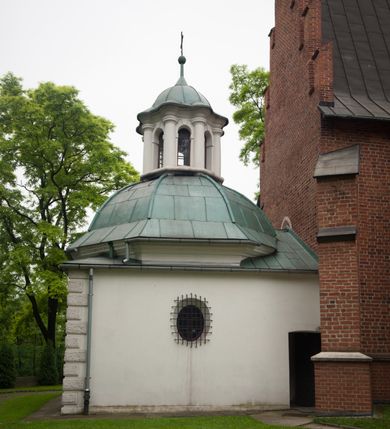 Zdjęcie nr 45: Na miejscu kościoła romańskiego, orientowany, dwunawowy, halowy; nawa południowa na rzucie prostokąta, na osi prezbiterium, dwuprzęsłowa, sklepiona kolebkowo z lunetami, na gurtach; nawa północna węższa od południowej, dwuprzęsłowa, sklepiona krzyżowo-żebrowo z kolistymi płaskorzeźbionymi zwornikami, jeden z literami ihs, drugi z literą s pod koroną. Prezbiterium prostokątne, dwuprzęsłowe, sklepione krzyżowo-żebrowo, z kolistymi zwornikami i profilowanymi wspornikami; przy nim od północy dawna zakrystia na rzucie prostokąta, sklepiona kolebkowo, otwarta do nawy wtórną arkadą, od wschodu nowa zakrystia na rzucie ośmioboku. Od zachodu przylega do nawy kwadratowa, czterokondygnacyjna wieża, z wieżyczką schodową w narożu północno-wschodnim, kruchtą w przyziemiu i chórem muzycznym na piętrze. Przy niej od północy drewniana piętrowa przybudówka mieszcząca w przyziemiu komorę bracką, na piętrze miech i kanał organowy. Przy nawie południowej od południa kwadratowa kruchta. Arkada tęczy zamknięta łukiem półkolistym, arkady do nawy północnej łukiem lekko zaostrzonym. Mury opięte przyporami, elewacje na cokole, z wzorami z zendrówki. Okna pierwotnie ostrołukowe, obustronnie rozglifione (niektóre zbarokizowane). Portale: zachodni, do kruchty pod wieżą, oraz do kruchty południowej, kamienne, prostokątne. Dachy dwuspadowe, pokryte blachą miedzianą. Zakrystia od wschodu przy prezbiterium wzniesiona na miejscu drewnianej kaplicy Ogrojcowej z XVIII wieku.