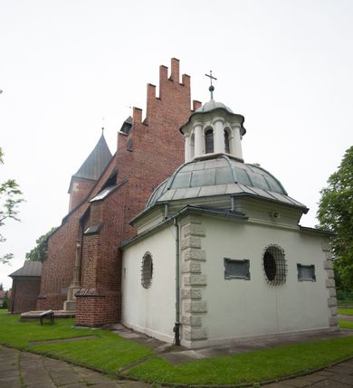 Zdjęcie nr 4: Na miejscu kościoła romańskiego, orientowany, dwunawowy, halowy; nawa południowa na rzucie prostokąta, na osi prezbiterium, dwuprzęsłowa, sklepiona kolebkowo z lunetami, na gurtach; nawa północna węższa od południowej, dwuprzęsłowa, sklepiona krzyżowo-żebrowo z kolistymi płaskorzeźbionymi zwornikami, jeden z literami ihs, drugi z literą s pod koroną. Prezbiterium prostokątne, dwuprzęsłowe, sklepione krzyżowo-żebrowo, z kolistymi zwornikami i profilowanymi wspornikami; przy nim od północy dawna zakrystia na rzucie prostokąta, sklepiona kolebkowo, otwarta do nawy wtórną arkadą, od wschodu nowa zakrystia na rzucie ośmioboku. Od zachodu przylega do nawy kwadratowa, czterokondygnacyjna wieża, z wieżyczką schodową w narożu północno-wschodnim, kruchtą w przyziemiu i chórem muzycznym na piętrze. Przy niej od północy drewniana piętrowa przybudówka mieszcząca w przyziemiu komorę bracką, na piętrze miech i kanał organowy. Przy nawie południowej od południa kwadratowa kruchta. Arkada tęczy zamknięta łukiem półkolistym, arkady do nawy północnej łukiem lekko zaostrzonym. Mury opięte przyporami, elewacje na cokole, z wzorami z zendrówki. Okna pierwotnie ostrołukowe, obustronnie rozglifione (niektóre zbarokizowane). Portale: zachodni, do kruchty pod wieżą, oraz do kruchty południowej, kamienne, prostokątne. Dachy dwuspadowe, pokryte blachą miedzianą. Zakrystia od wschodu przy prezbiterium wzniesiona na miejscu drewnianej kaplicy Ogrojcowej z XVIII wieku.