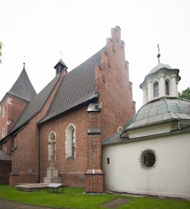 Zdjęcie nr 5: Na miejscu kościoła romańskiego, orientowany, dwunawowy, halowy; nawa południowa na rzucie prostokąta, na osi prezbiterium, dwuprzęsłowa, sklepiona kolebkowo z lunetami, na gurtach; nawa północna węższa od południowej, dwuprzęsłowa, sklepiona krzyżowo-żebrowo z kolistymi płaskorzeźbionymi zwornikami, jeden z literami ihs, drugi z literą s pod koroną. Prezbiterium prostokątne, dwuprzęsłowe, sklepione krzyżowo-żebrowo, z kolistymi zwornikami i profilowanymi wspornikami; przy nim od północy dawna zakrystia na rzucie prostokąta, sklepiona kolebkowo, otwarta do nawy wtórną arkadą, od wschodu nowa zakrystia na rzucie ośmioboku. Od zachodu przylega do nawy kwadratowa, czterokondygnacyjna wieża, z wieżyczką schodową w narożu północno-wschodnim, kruchtą w przyziemiu i chórem muzycznym na piętrze. Przy niej od północy drewniana piętrowa przybudówka mieszcząca w przyziemiu komorę bracką, na piętrze miech i kanał organowy. Przy nawie południowej od południa kwadratowa kruchta. Arkada tęczy zamknięta łukiem półkolistym, arkady do nawy północnej łukiem lekko zaostrzonym. Mury opięte przyporami, elewacje na cokole, z wzorami z zendrówki. Okna pierwotnie ostrołukowe, obustronnie rozglifione (niektóre zbarokizowane). Portale: zachodni, do kruchty pod wieżą, oraz do kruchty południowej, kamienne, prostokątne. Dachy dwuspadowe, pokryte blachą miedzianą. Zakrystia od wschodu przy prezbiterium wzniesiona na miejscu drewnianej kaplicy Ogrojcowej z XVIII wieku.