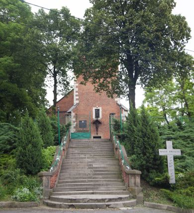 Zdjęcie nr 13: Na miejscu kościoła romańskiego, orientowany, dwunawowy, halowy; nawa południowa na rzucie prostokąta, na osi prezbiterium, dwuprzęsłowa, sklepiona kolebkowo z lunetami, na gurtach; nawa północna węższa od południowej, dwuprzęsłowa, sklepiona krzyżowo-żebrowo z kolistymi płaskorzeźbionymi zwornikami, jeden z literami ihs, drugi z literą s pod koroną. Prezbiterium prostokątne, dwuprzęsłowe, sklepione krzyżowo-żebrowo, z kolistymi zwornikami i profilowanymi wspornikami; przy nim od północy dawna zakrystia na rzucie prostokąta, sklepiona kolebkowo, otwarta do nawy wtórną arkadą, od wschodu nowa zakrystia na rzucie ośmioboku. Od zachodu przylega do nawy kwadratowa, czterokondygnacyjna wieża, z wieżyczką schodową w narożu północno-wschodnim, kruchtą w przyziemiu i chórem muzycznym na piętrze. Przy niej od północy drewniana piętrowa przybudówka mieszcząca w przyziemiu komorę bracką, na piętrze miech i kanał organowy. Przy nawie południowej od południa kwadratowa kruchta. Arkada tęczy zamknięta łukiem półkolistym, arkady do nawy północnej łukiem lekko zaostrzonym. Mury opięte przyporami, elewacje na cokole, z wzorami z zendrówki. Okna pierwotnie ostrołukowe, obustronnie rozglifione (niektóre zbarokizowane). Portale: zachodni, do kruchty pod wieżą, oraz do kruchty południowej, kamienne, prostokątne. Dachy dwuspadowe, pokryte blachą miedzianą. Zakrystia od wschodu przy prezbiterium wzniesiona na miejscu drewnianej kaplicy Ogrojcowej z XVIII wieku.